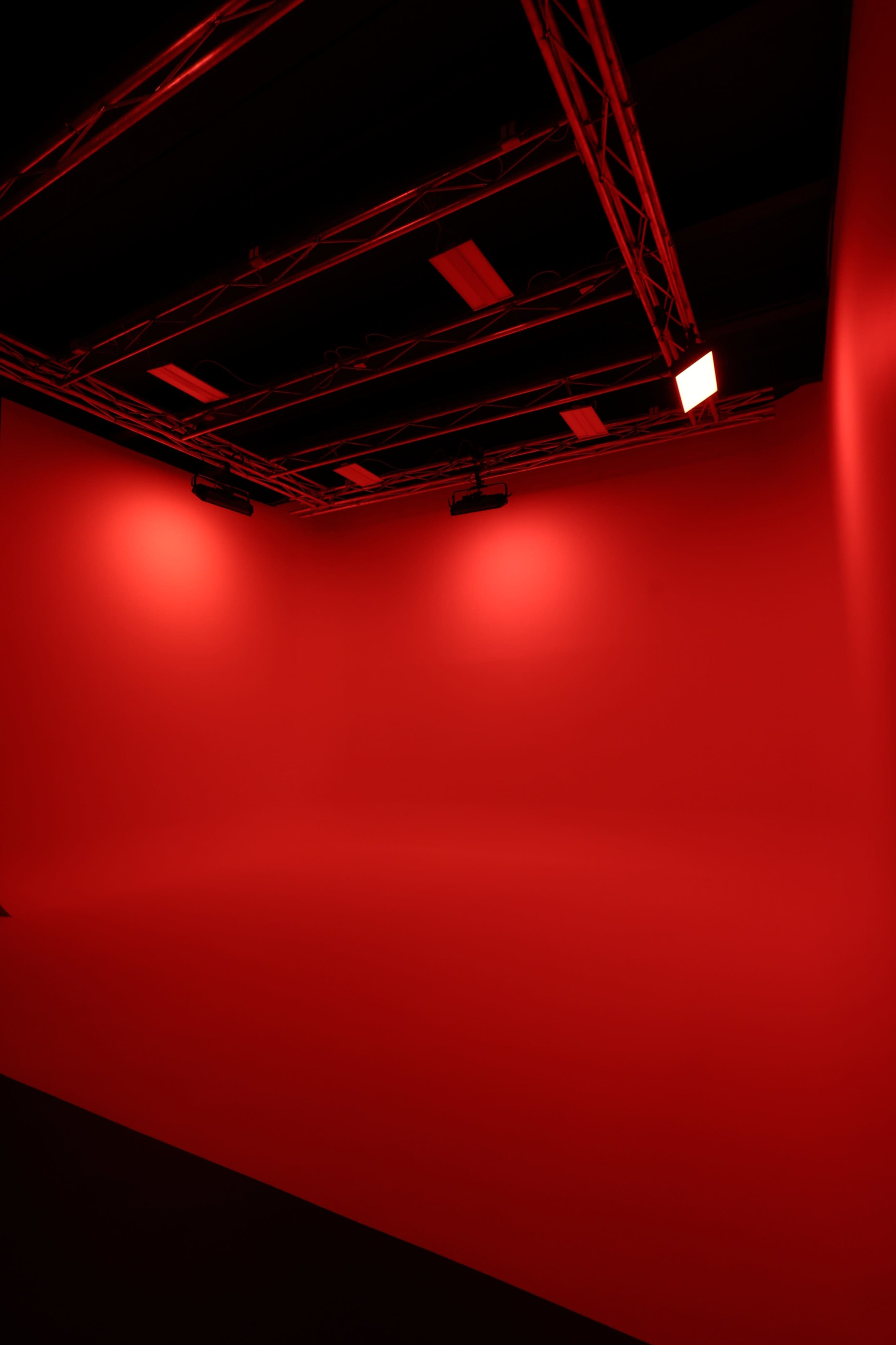 The image shows a dimly lit room with all red walls and a red floor, illuminated by several overhead lights.