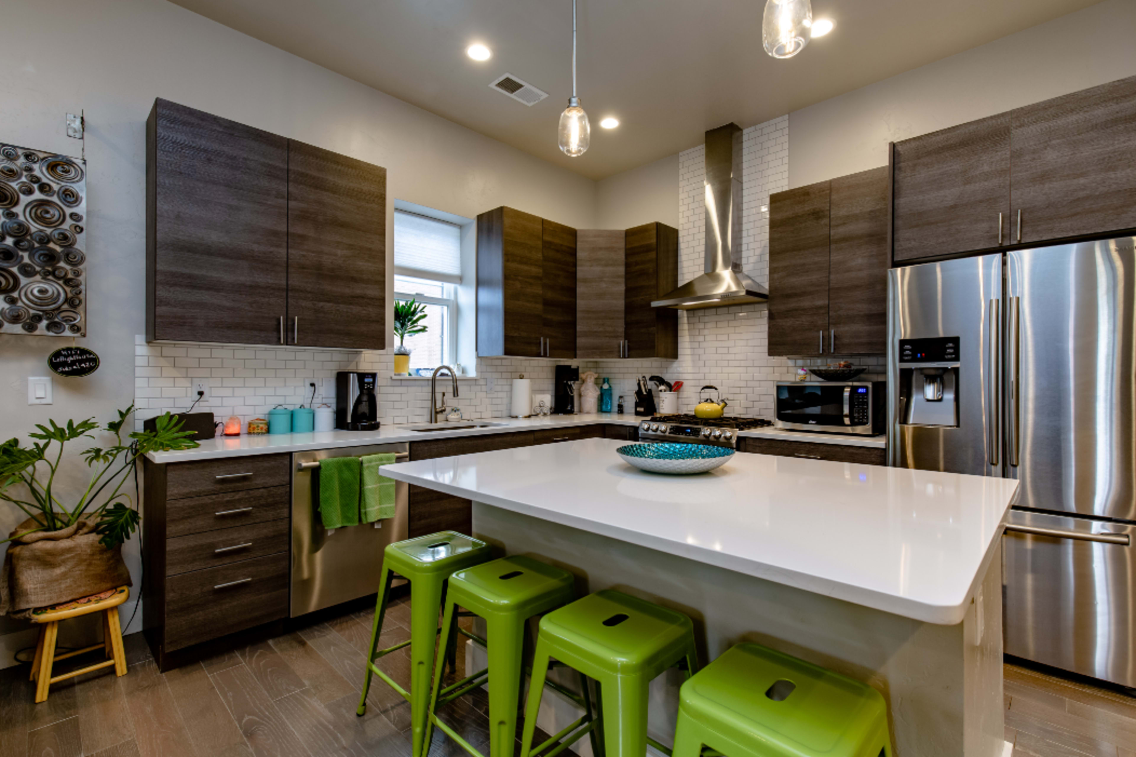 The kitchen features modern cabinetry, stainless steel appliances, and a central island with green stools.
