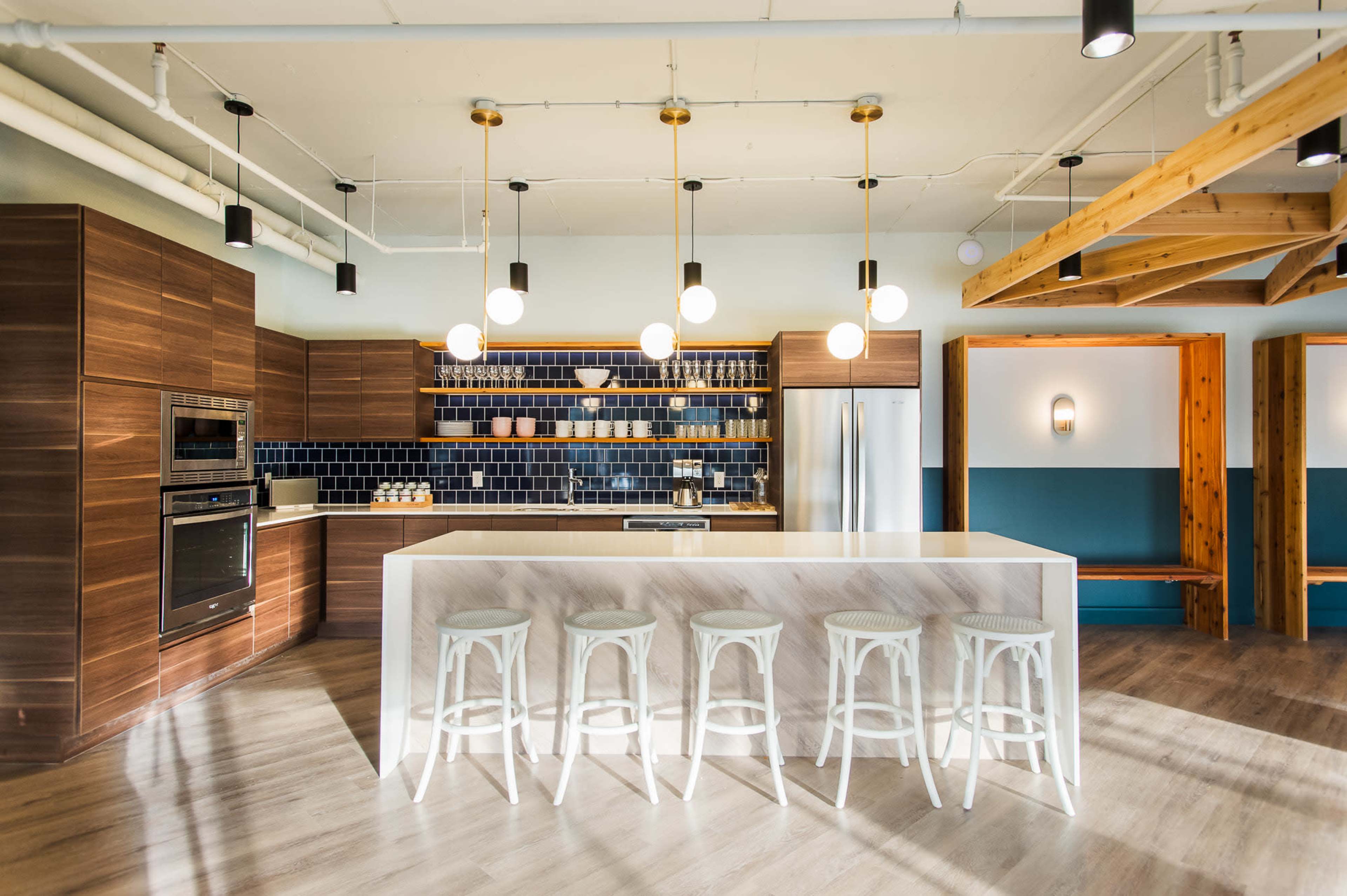 A modern kitchen with wooden cabinetry, a spacious island with white stools, and overhead pendant lights.