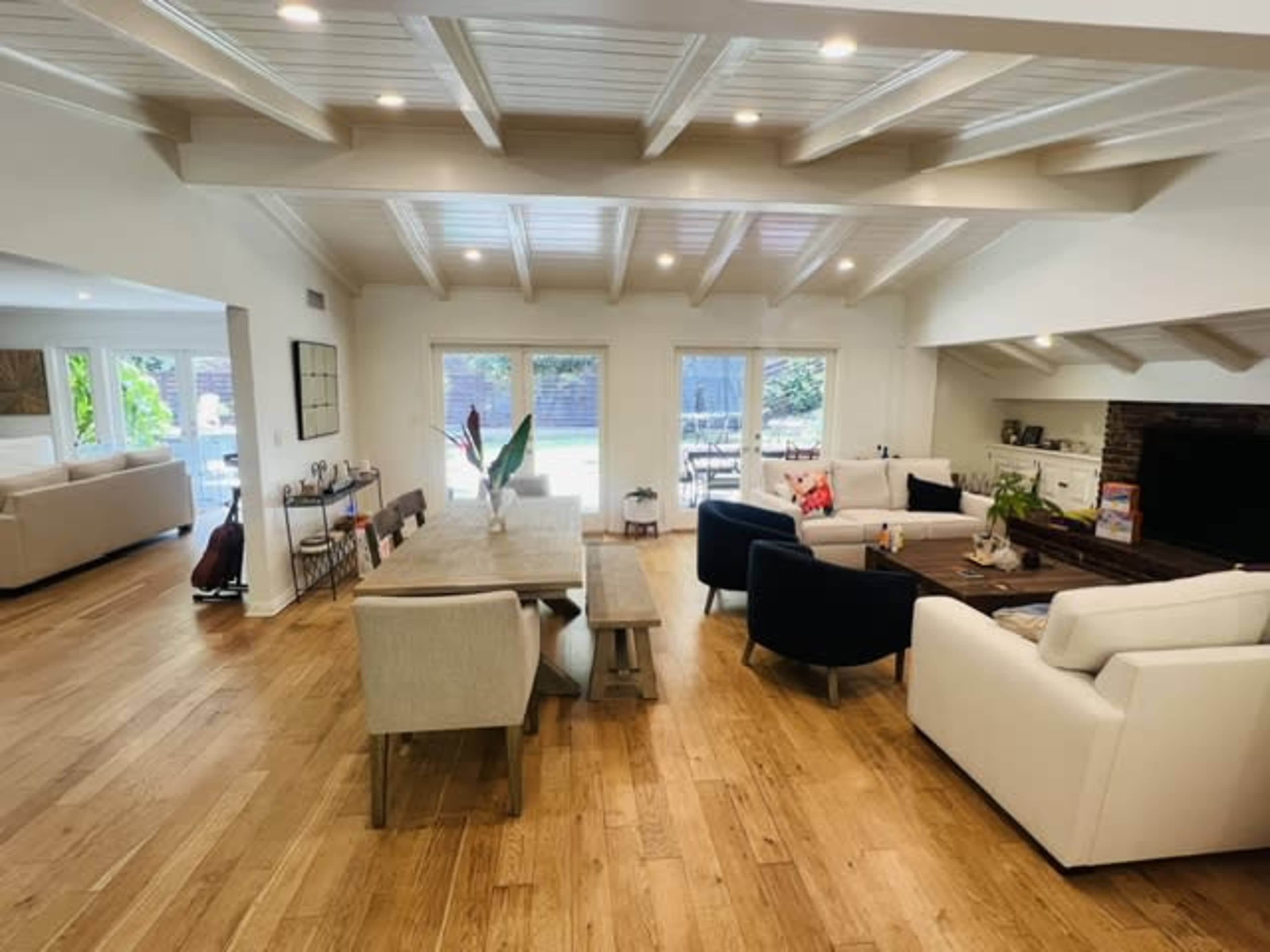 The image shows a modern, open-concept living area featuring a dining table, comfortable seating, and large windows that provide natural light.