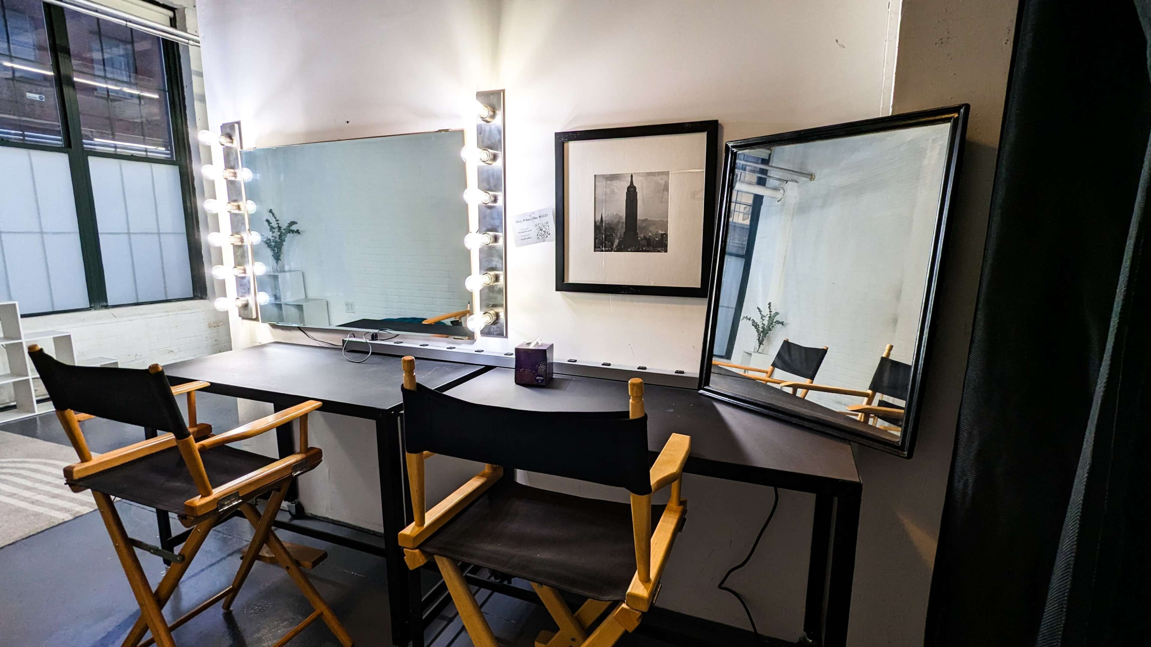 The image shows a well-lit makeup station with two director's chairs, a large mirror framed by lights, and additional mirrors reflecting the space.