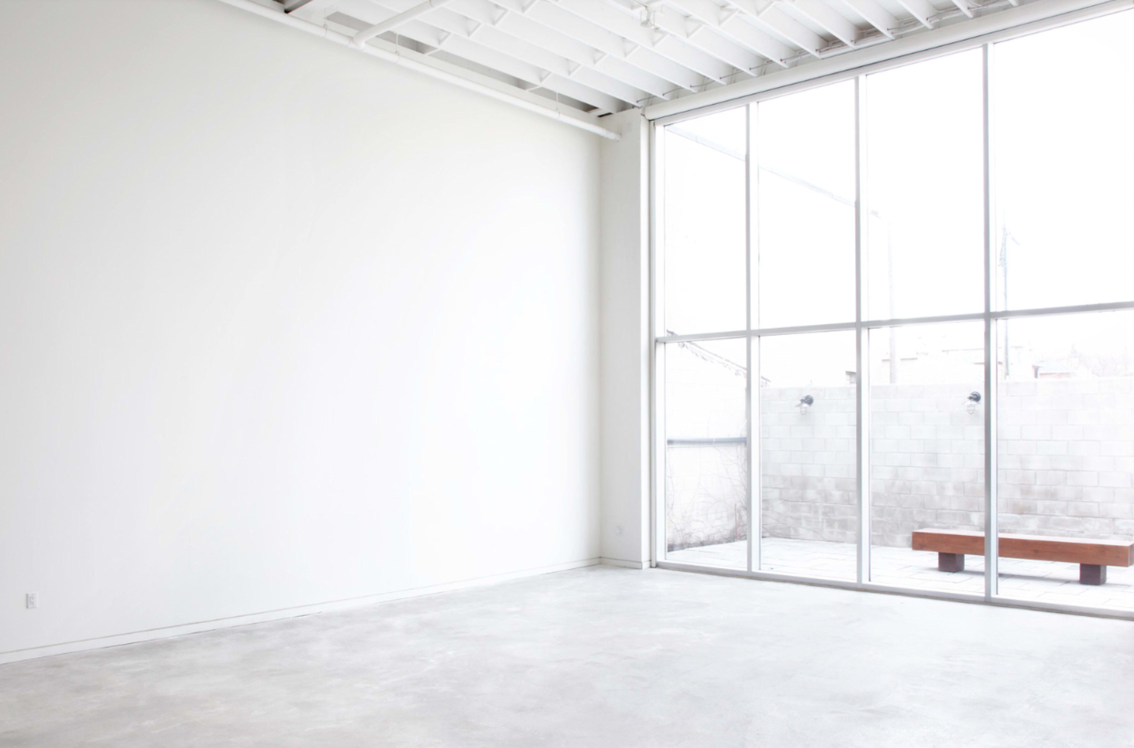 A spacious, bright room with a large window overlooking a small outdoor area and a minimalistic wooden bench.