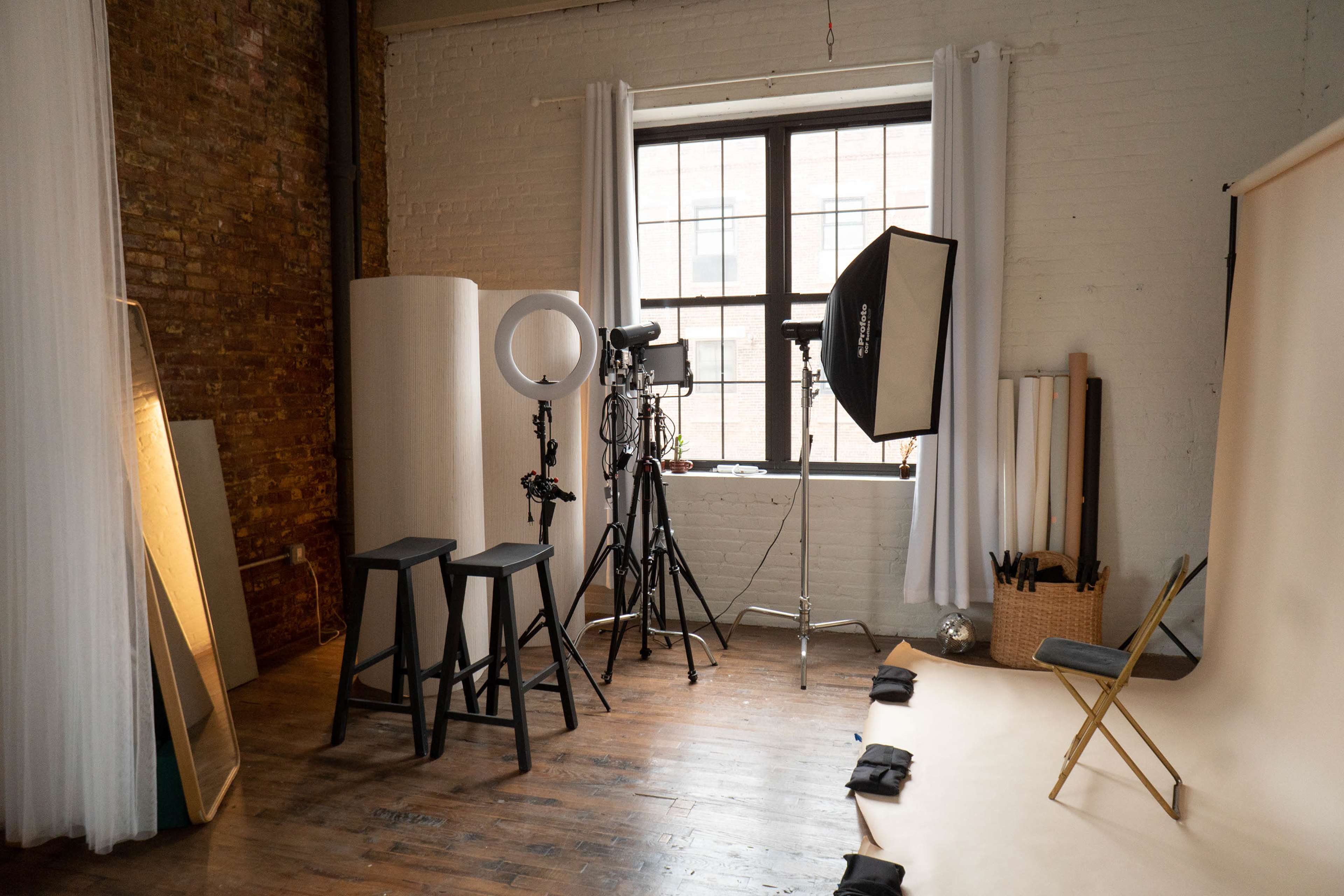 A photography studio setup with various lighting equipment, backdrops, and seating arrangements in a room with exposed brick walls and large windows.