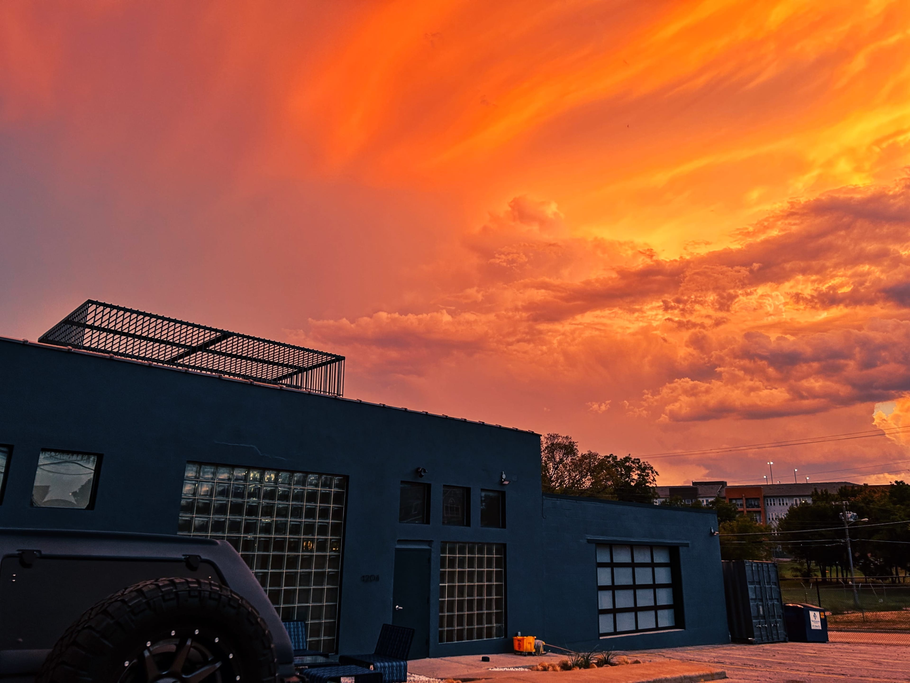 A dark blue building with large windows stands against a vibrant orange and purple sunset sky.