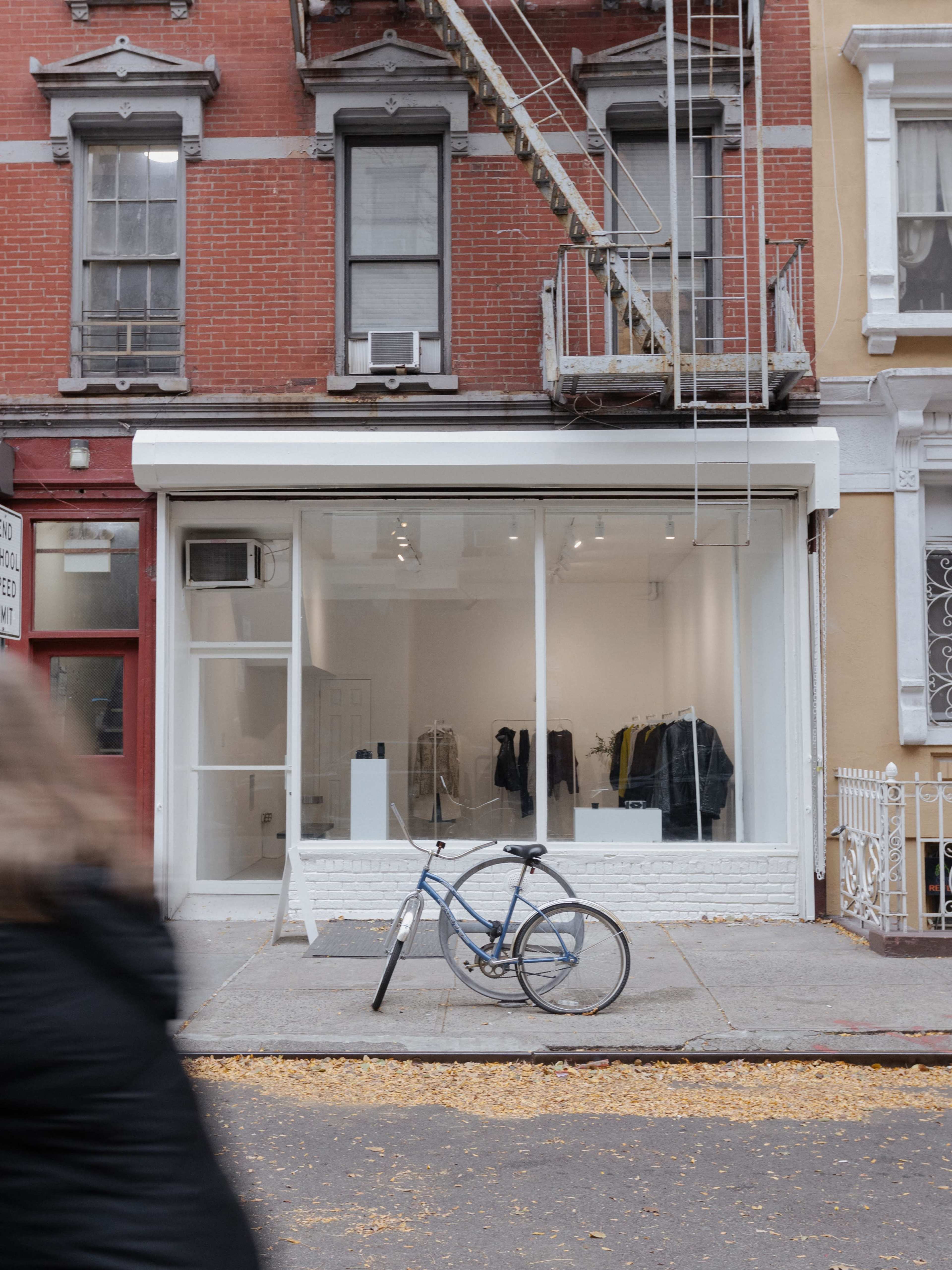 A blue bicycle is parked in front of a modern storefront with large glass windows displaying clothing on racks.
