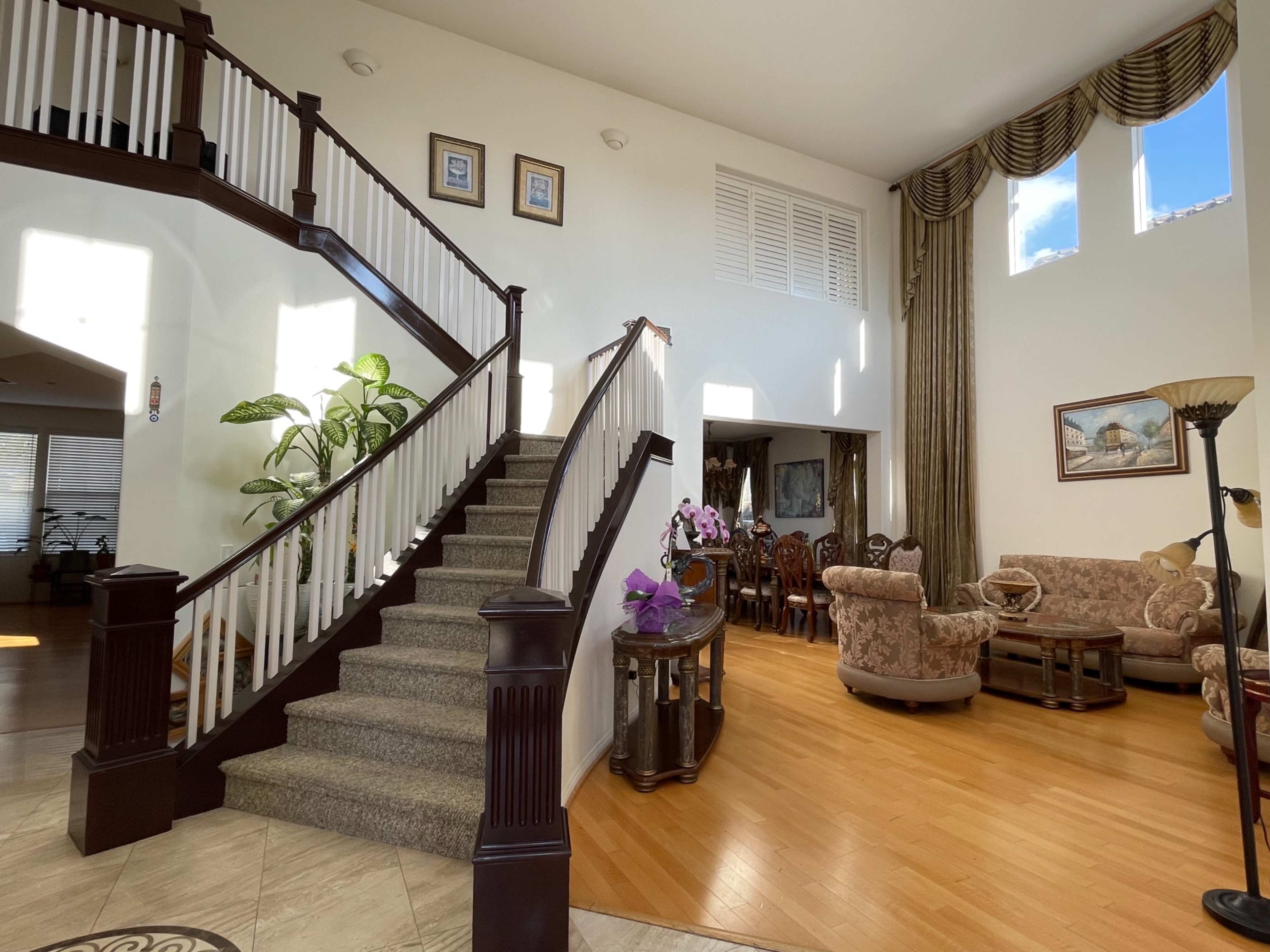 A spacious foyer with a staircase leading to an upper level, adjacent to a living area furnished with chairs and a large window.