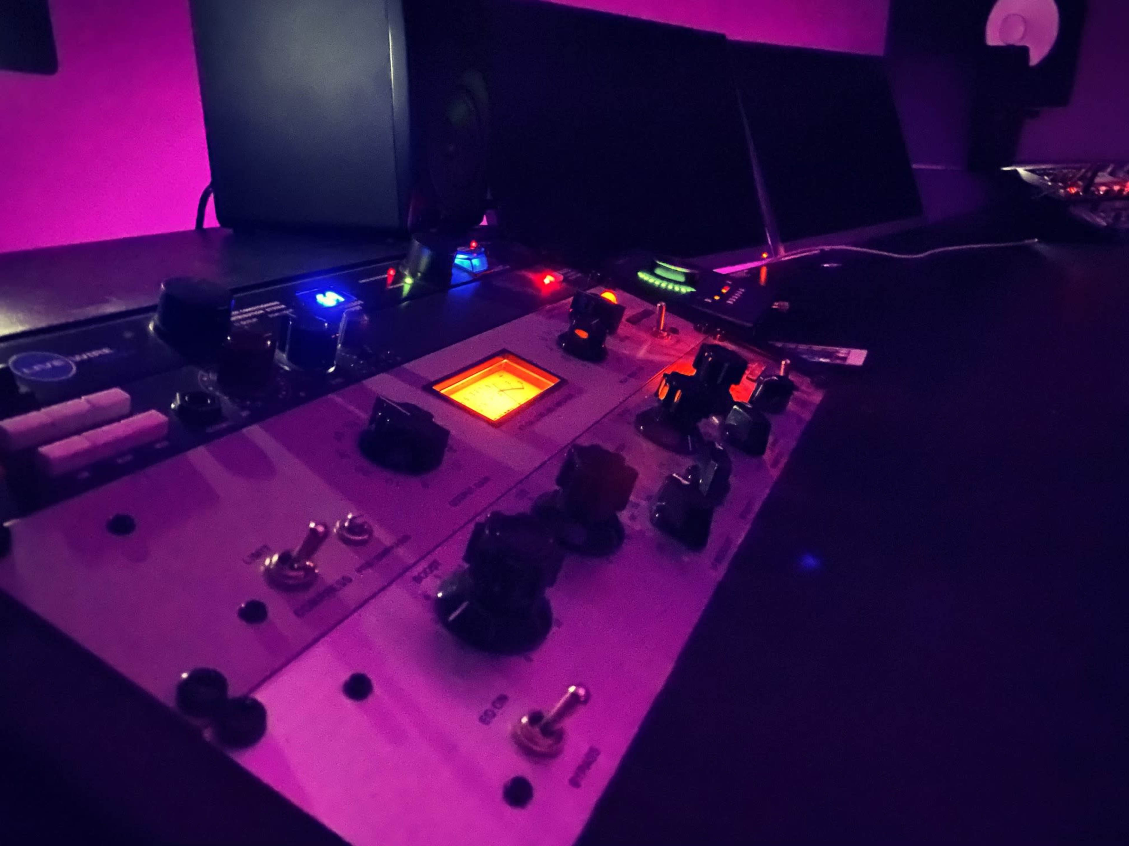A close-up of audio equipment with various knobs and lights on a dark surface in a studio setting.
