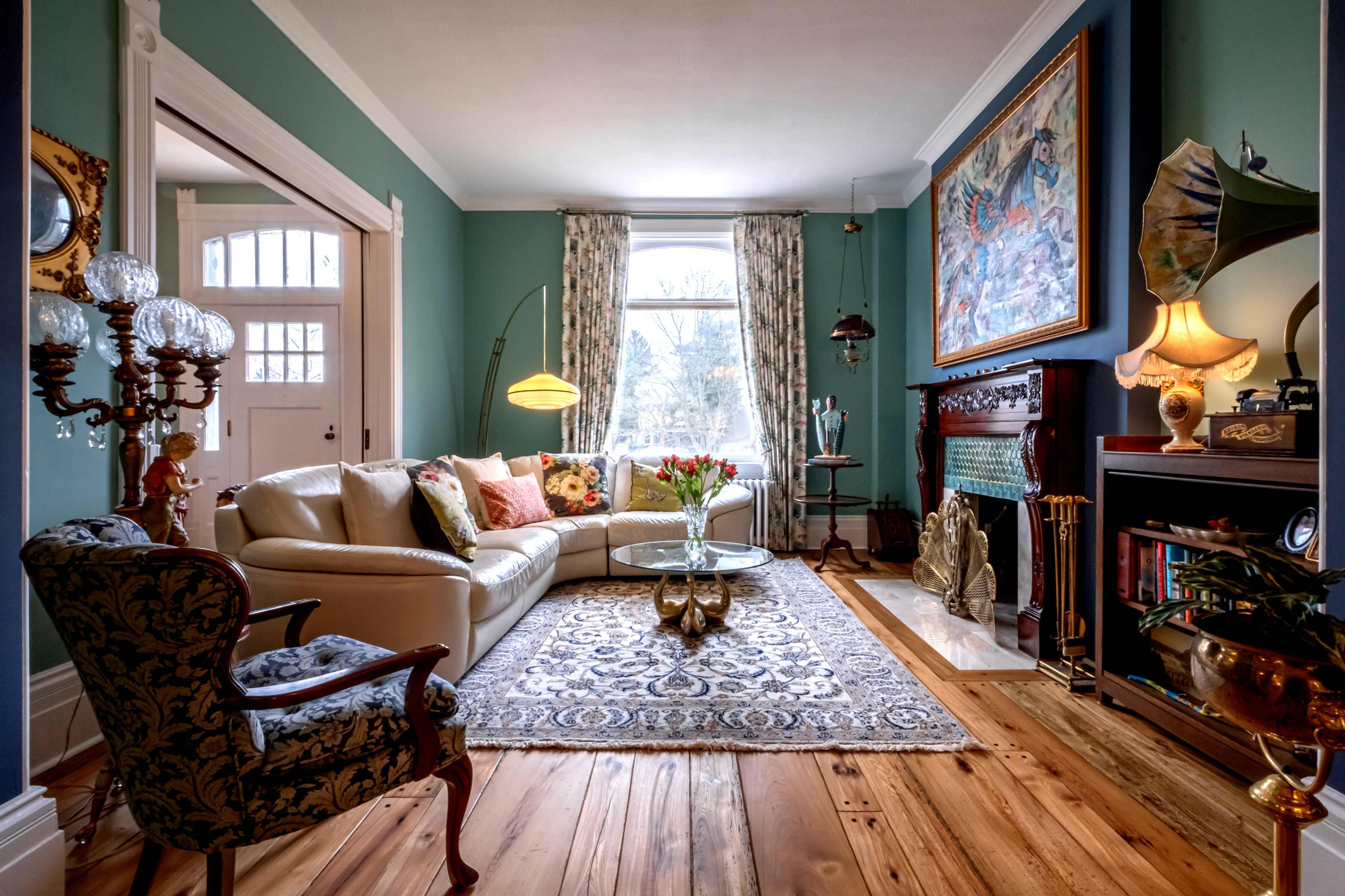 The living room features a cream-colored sofa, a glass coffee table, and a vintage fireplace, all set against a backdrop of teal walls and hardwood floors.