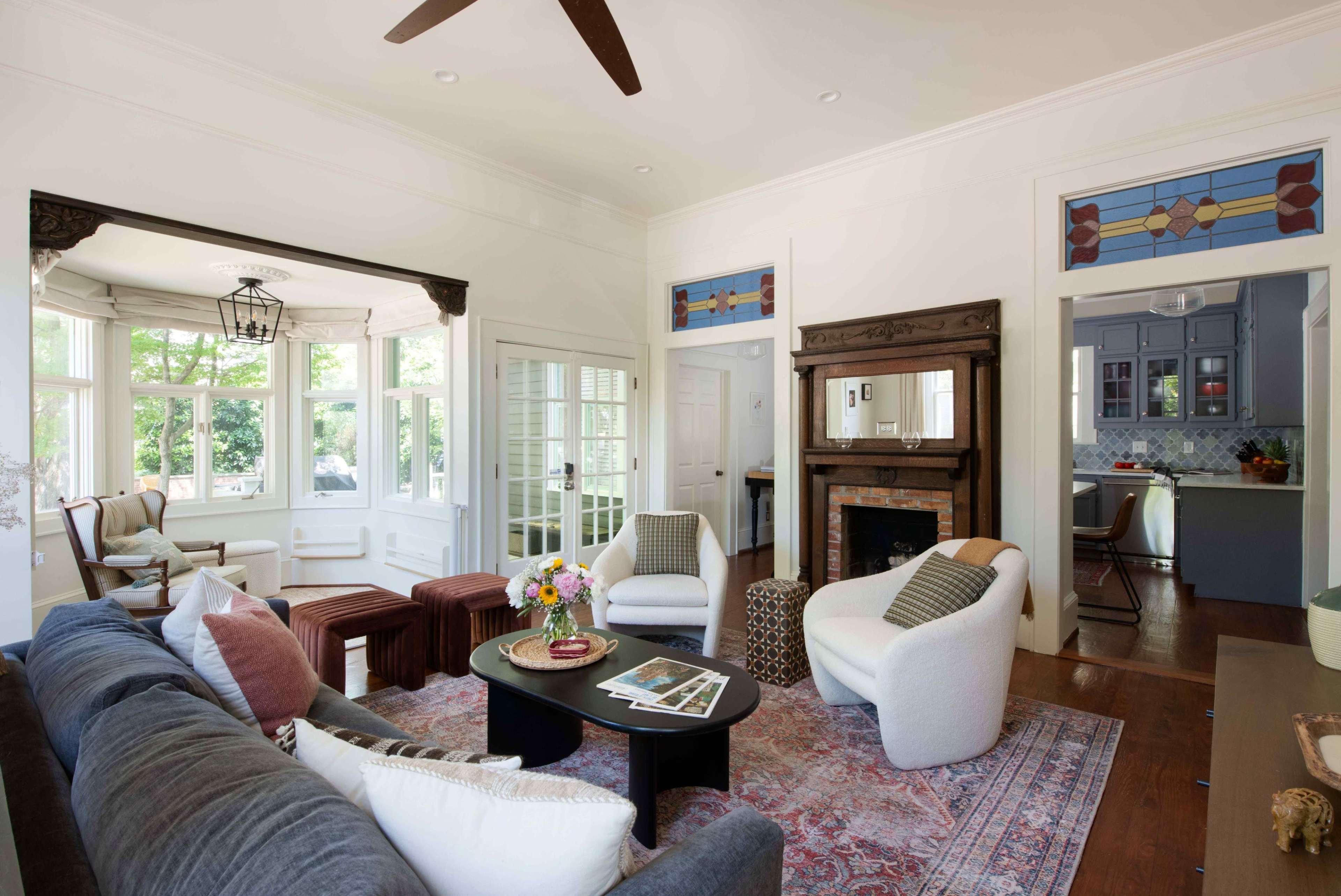 The image shows a bright living room with a seating area, a fireplace, and large windows that provide natural light.