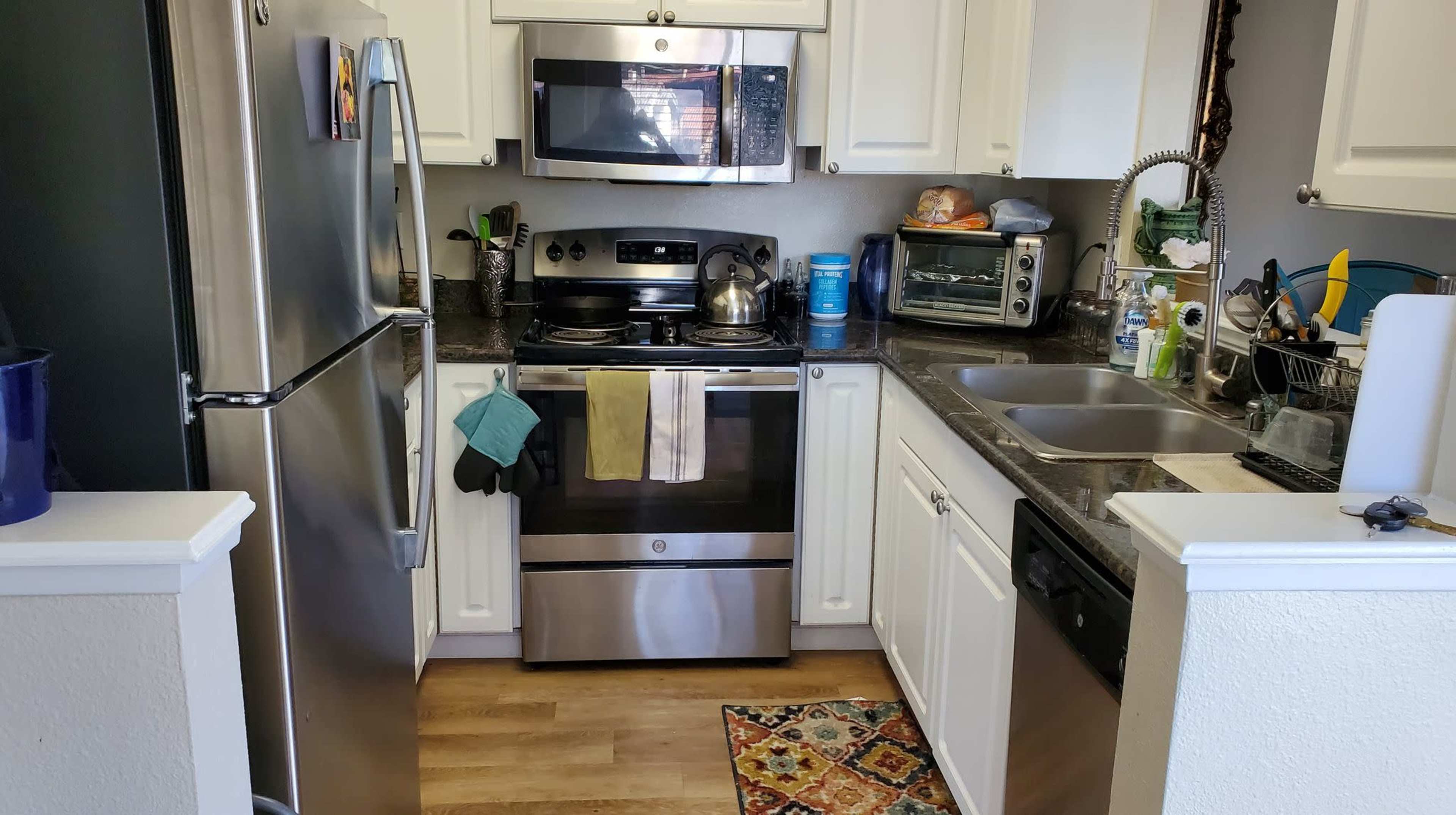 A kitchen featuring stainless steel appliances, white cabinetry, and a granite countertop, with a colorful rug on the floor.