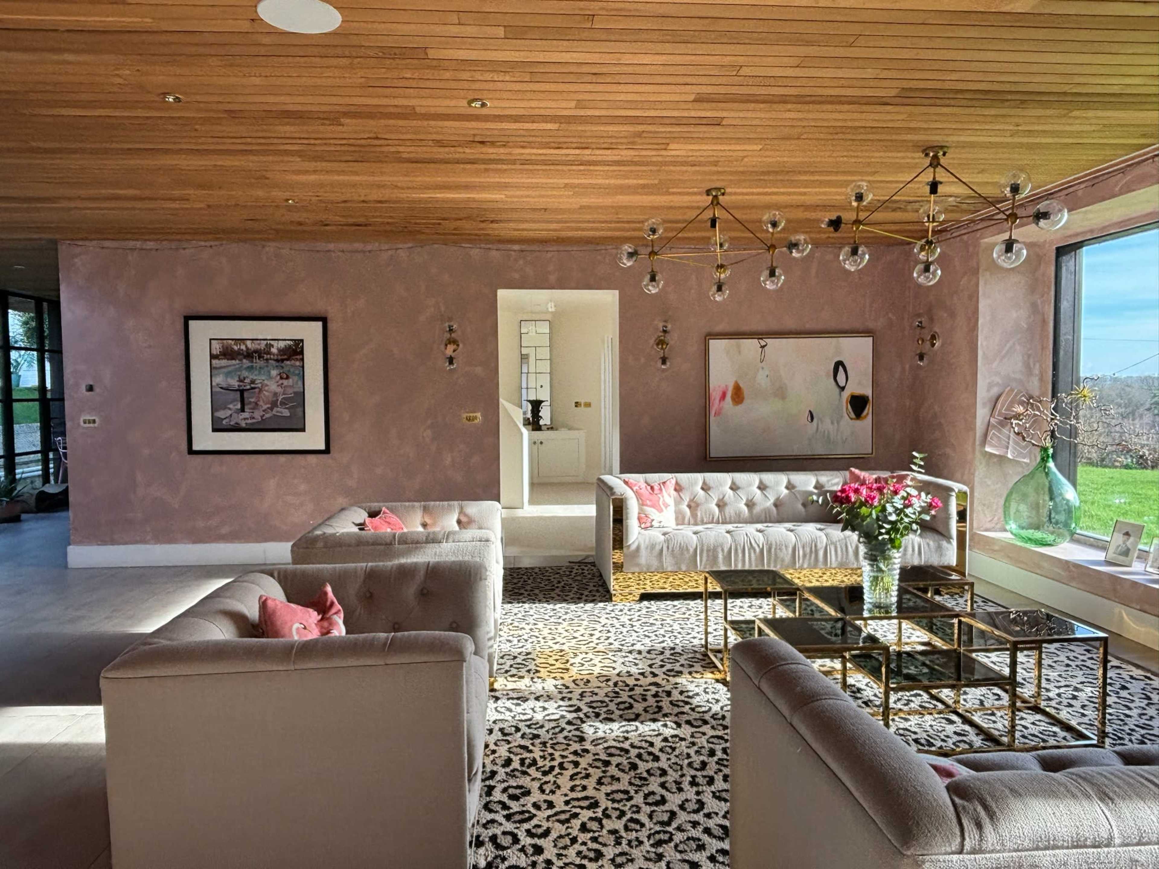 The living room features two tufted sofas, a glass coffee table atop a leopard-print rug, and large windows that provide natural light.