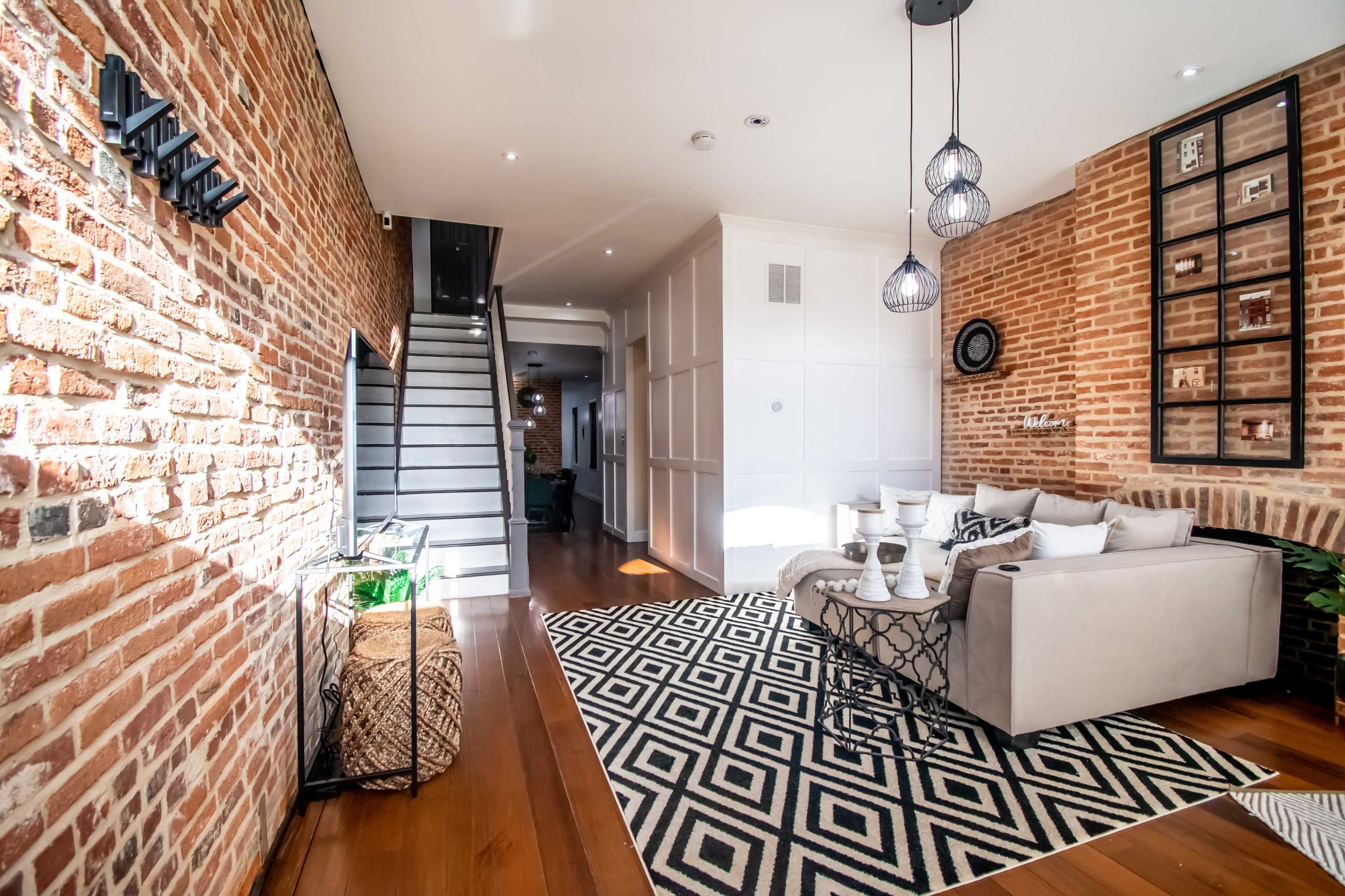 A modern living room with brick walls, a patterned rug, and a staircase in the background.