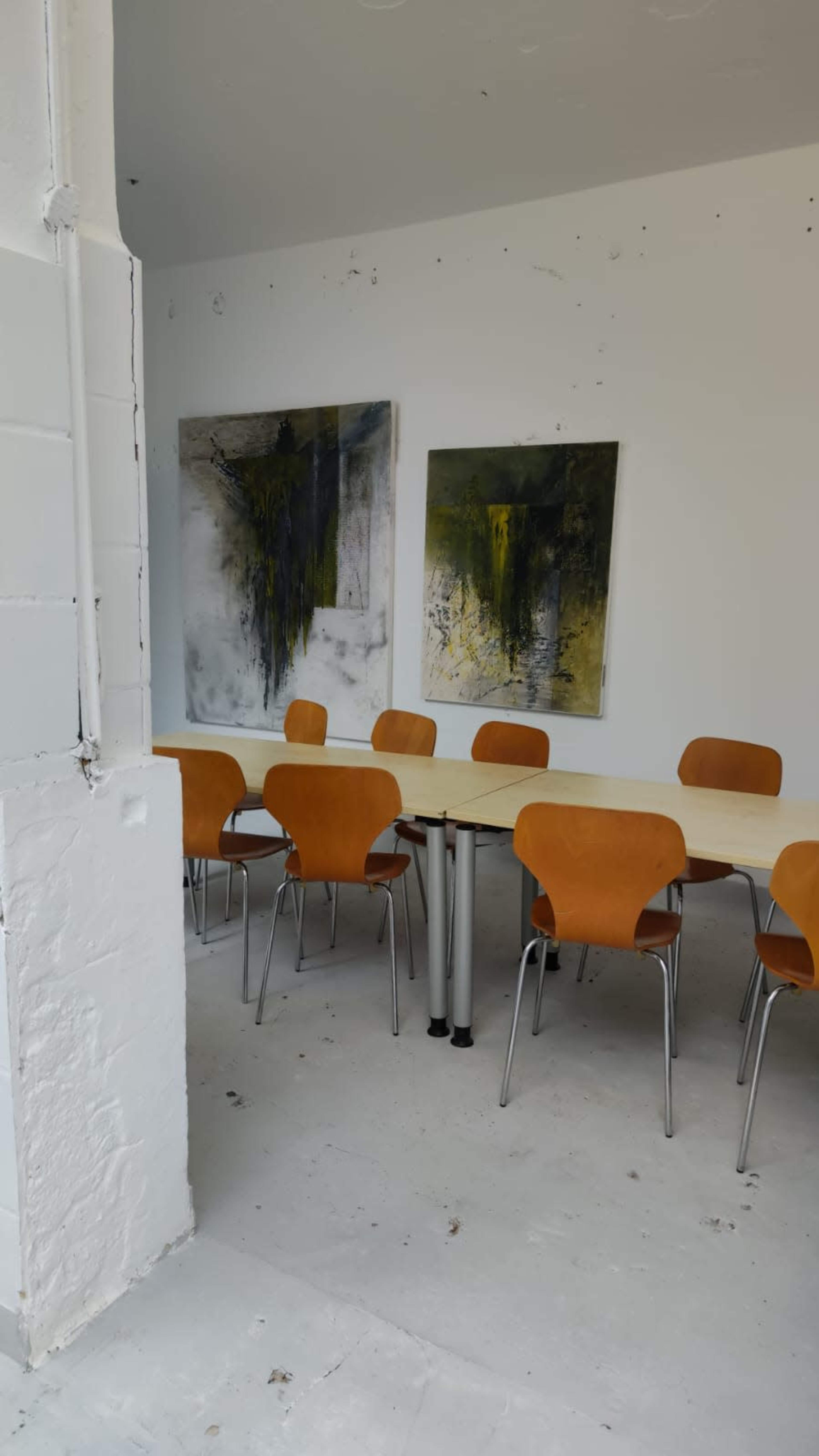 The image shows a meeting room with a long table surrounded by orange chairs and two large abstract paintings on the wall.