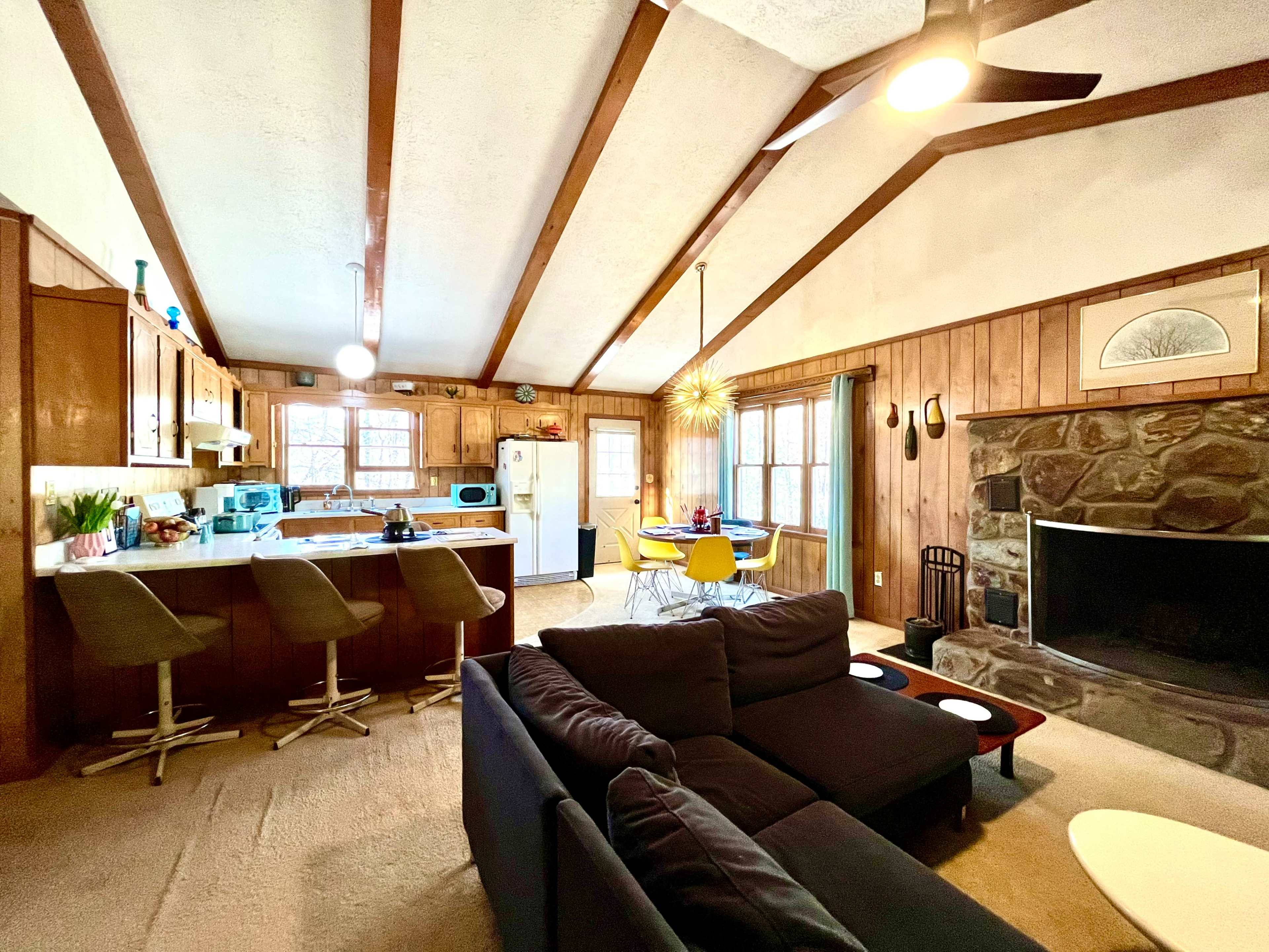 A spacious living area with a kitchen counter, a stone fireplace, and a cozy seating arrangement.