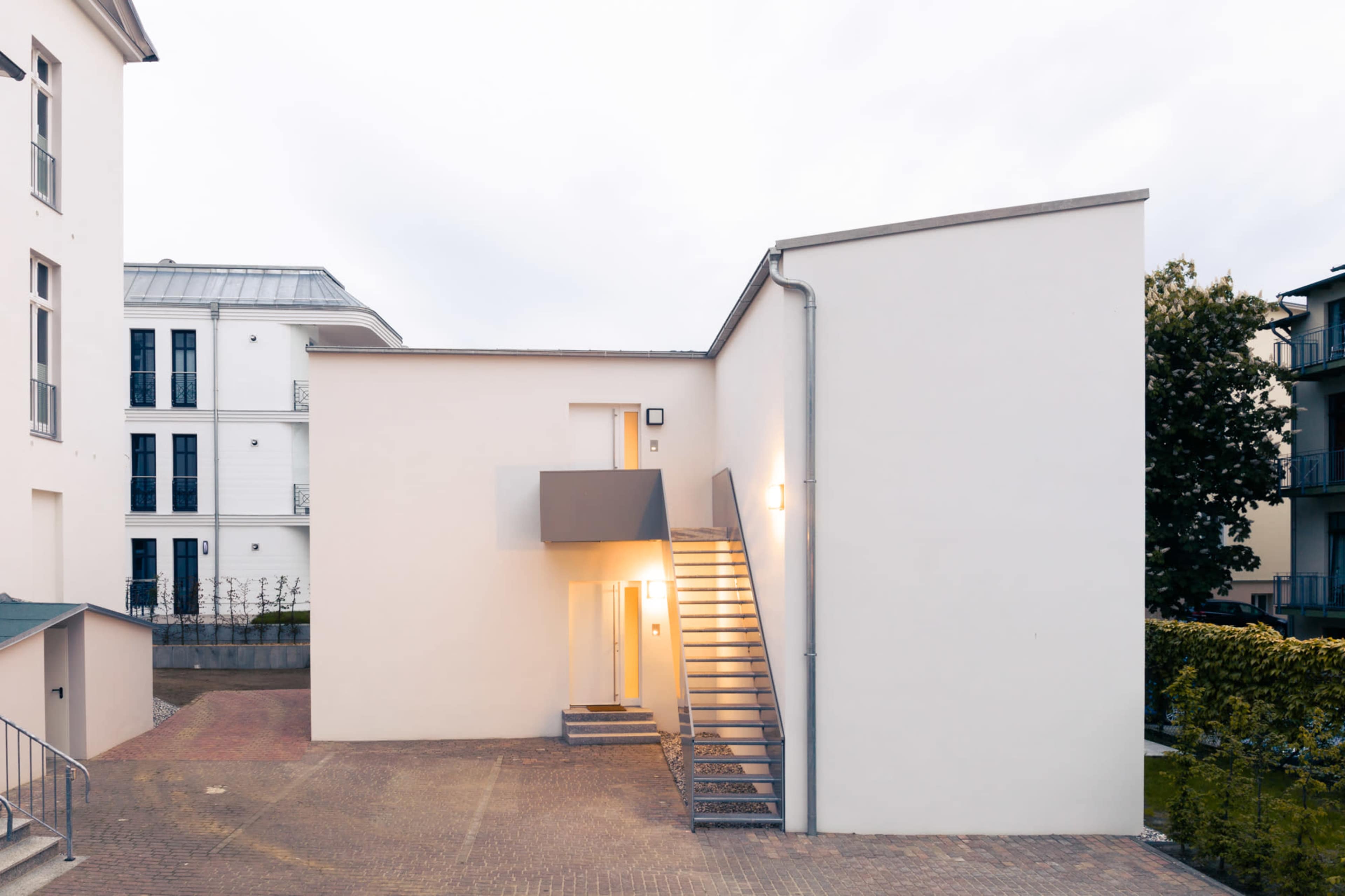 The image shows a modern building with a stairway leading to an upper entrance, surrounded by well-maintained grounds.