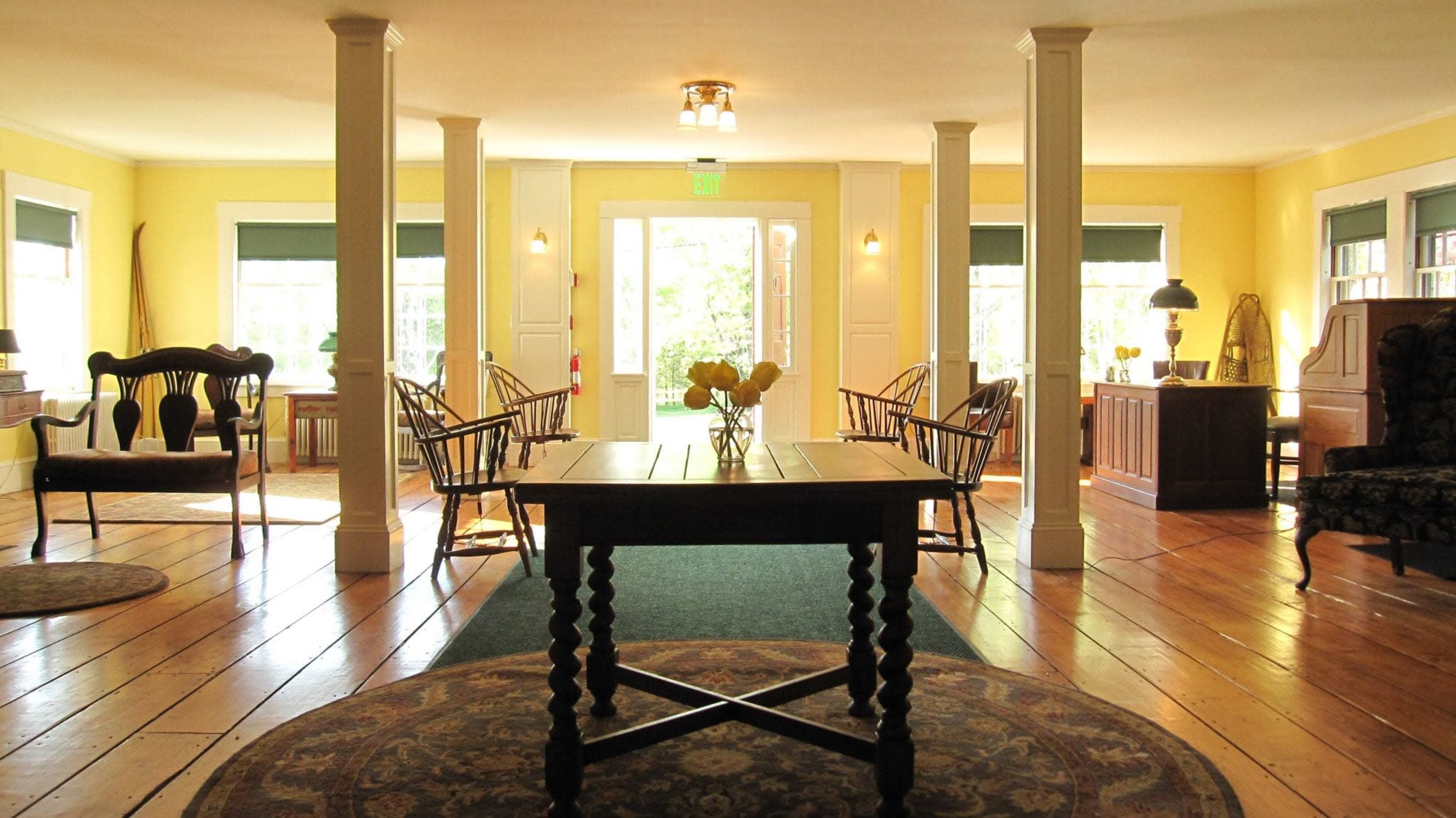A bright room with yellow walls, wooden flooring, and various seating arrangements around a central table.