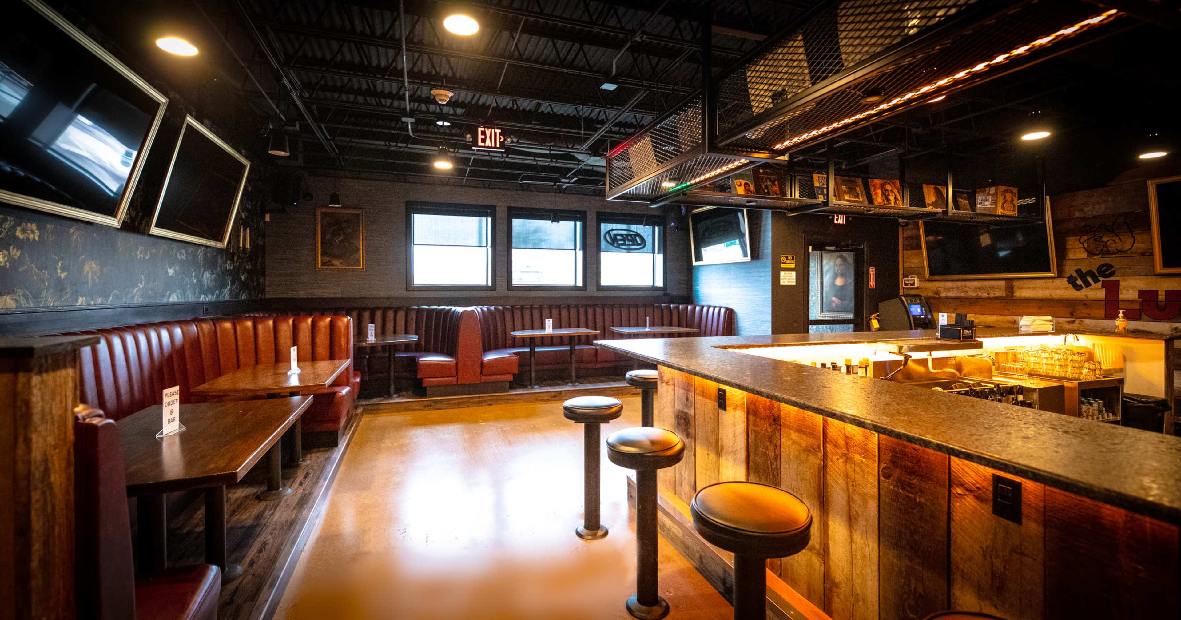The image shows the interior of a bar featuring leather booths, a wooden counter, and multiple televisions on the walls.