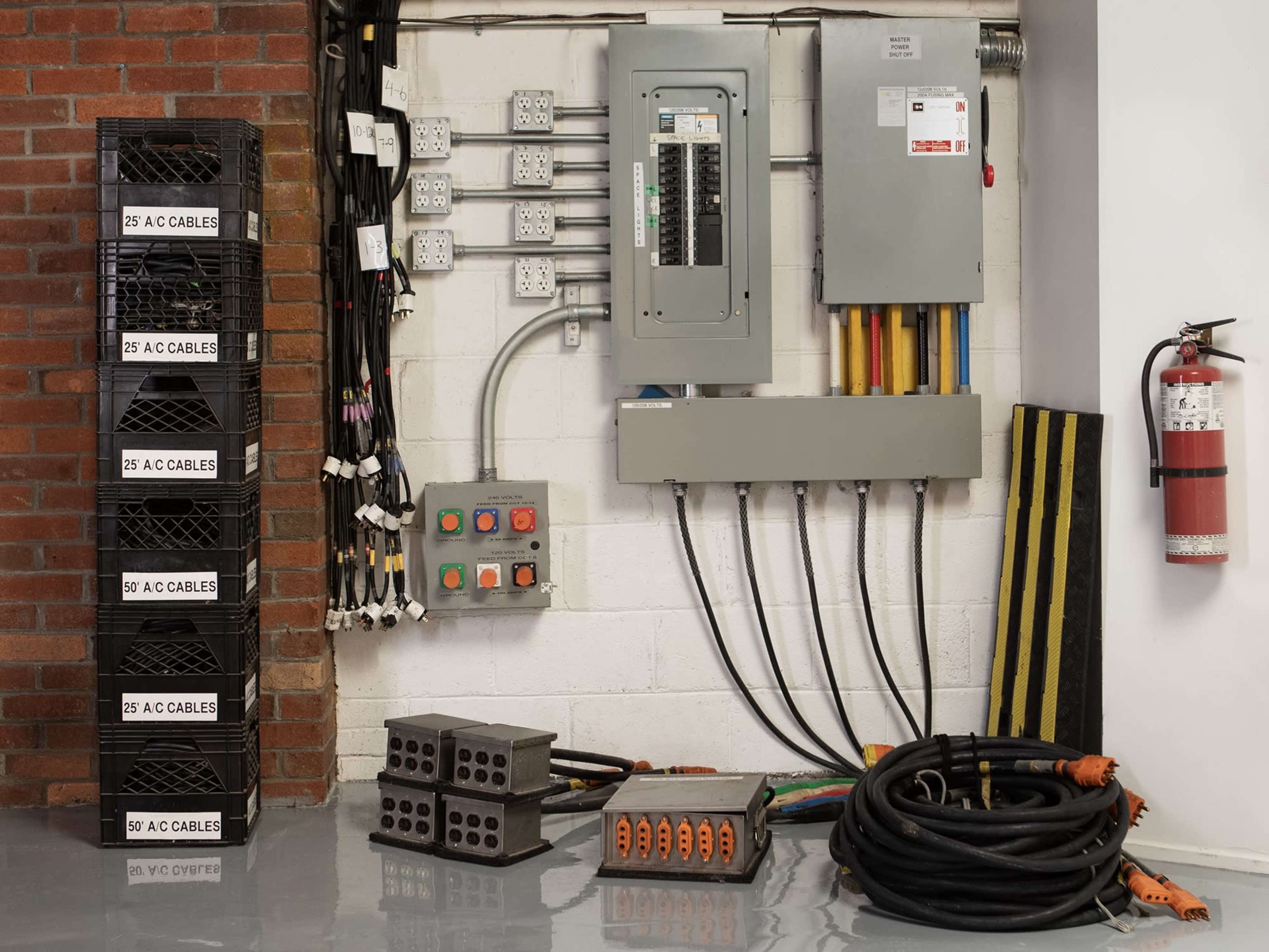 The image shows an electrical panel and related equipment, including power cables, outlets, and a fire extinguisher mounted on a wall.
