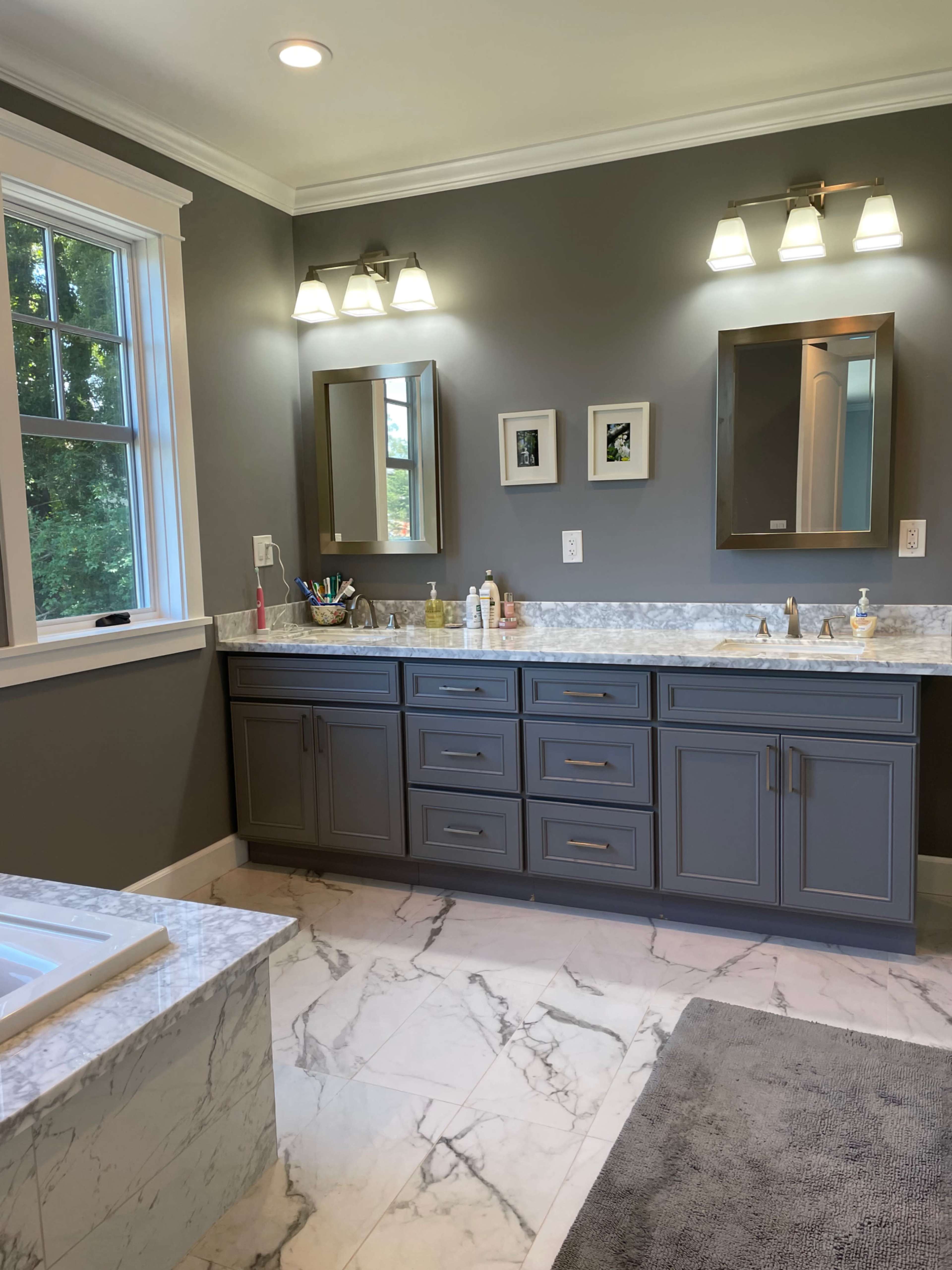 A modern bathroom with gray walls, a marble floor, and a double vanity with lighting fixtures and mirrors above it.
