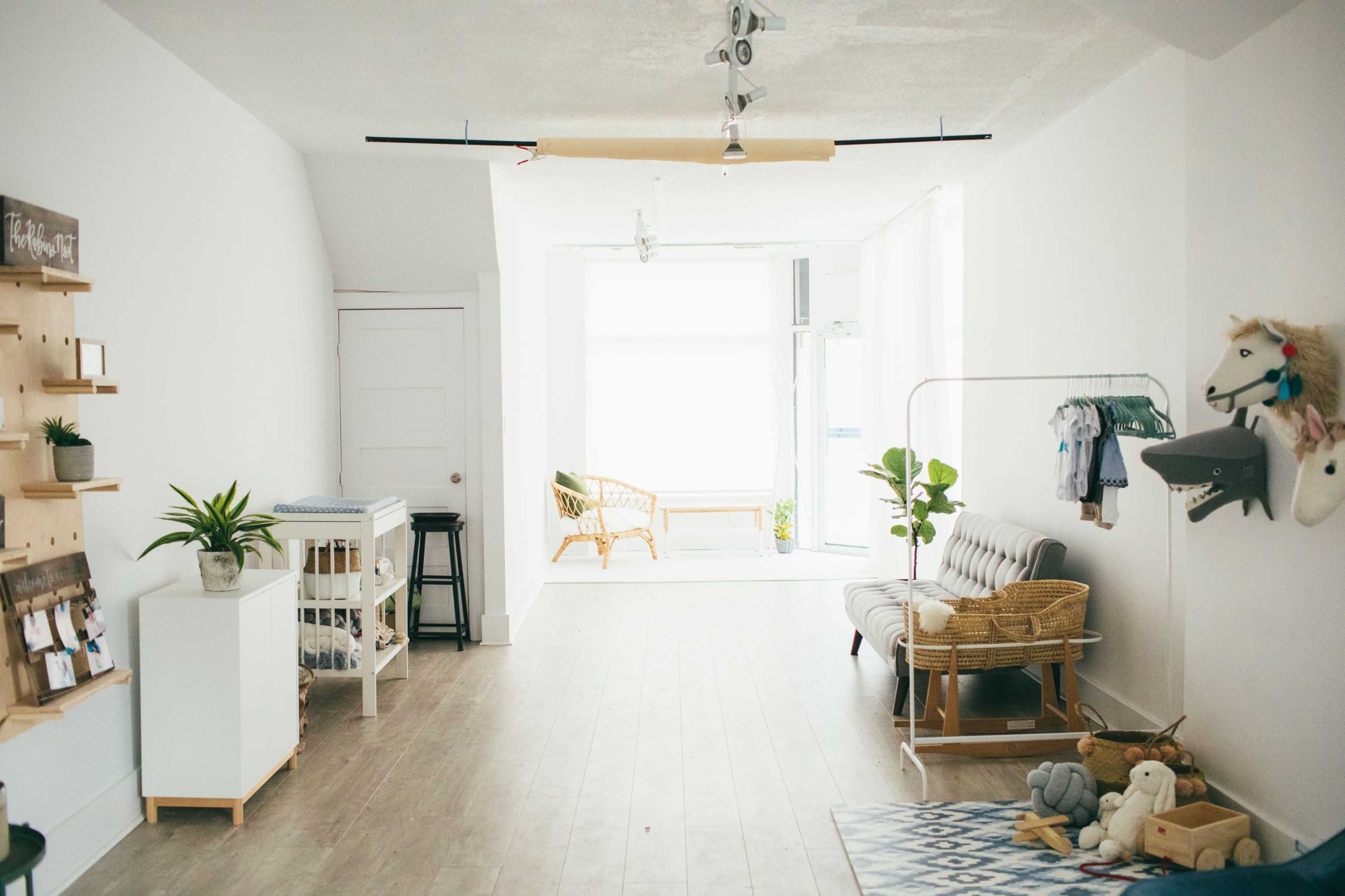 A bright, minimalist room with light wood flooring, featuring a seating area, a clothing rack, and various decor items on display.