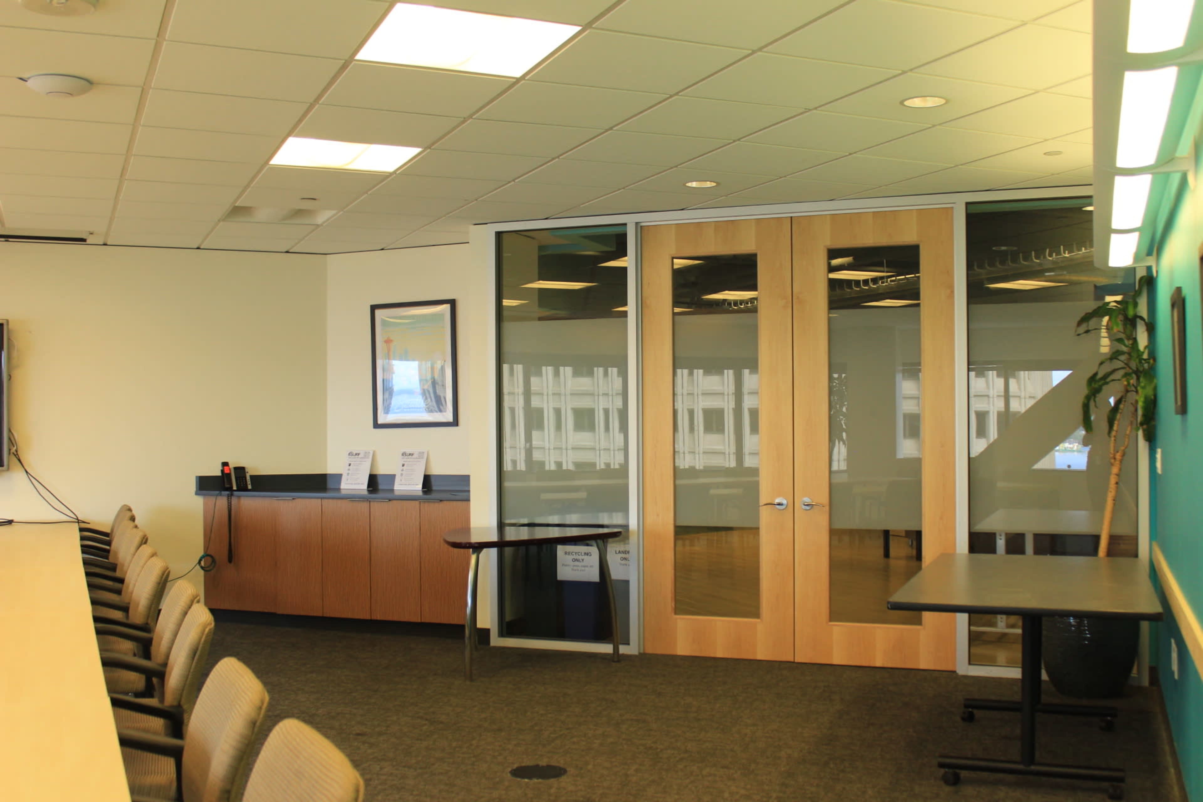 A modern conference room features glass doors, a long table with chairs, and a blue accent wall with a potted plant.