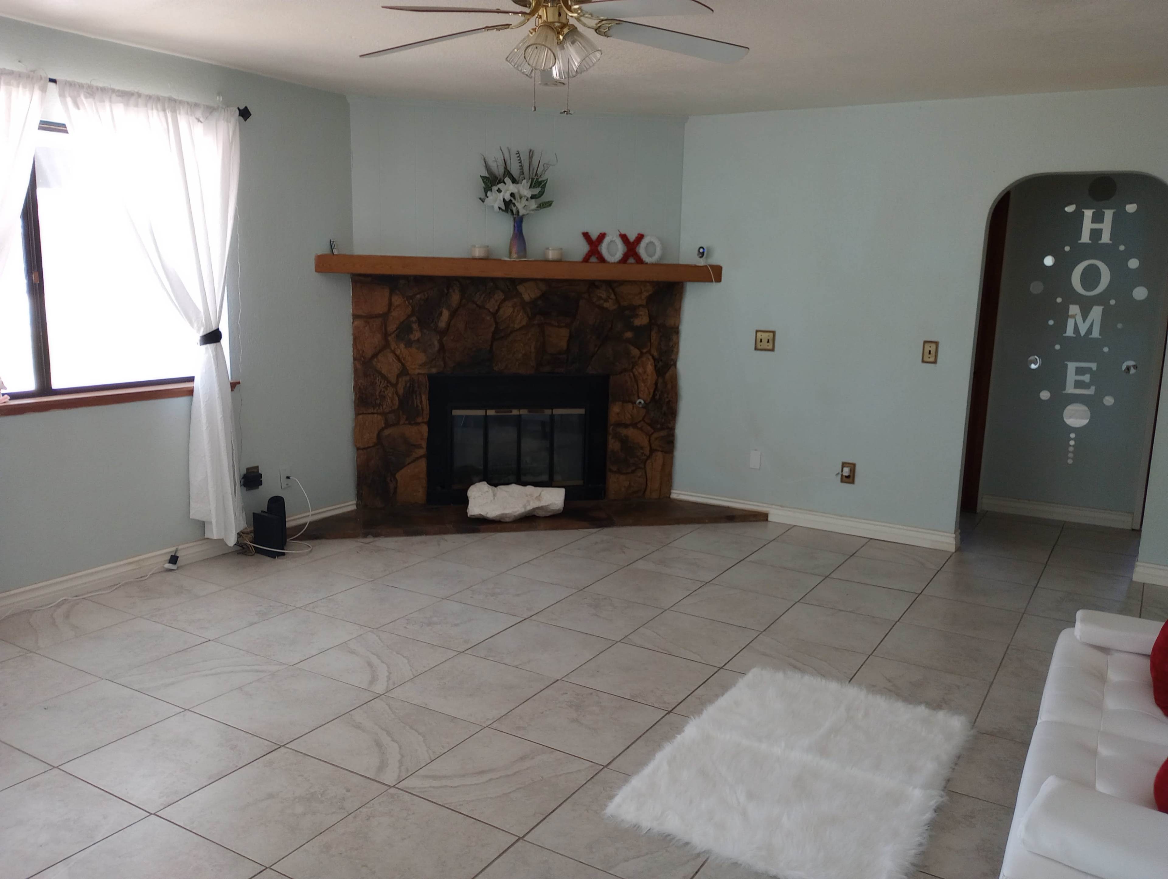The living room features a stone fireplace, light blue walls, and a white rug on tiled flooring.