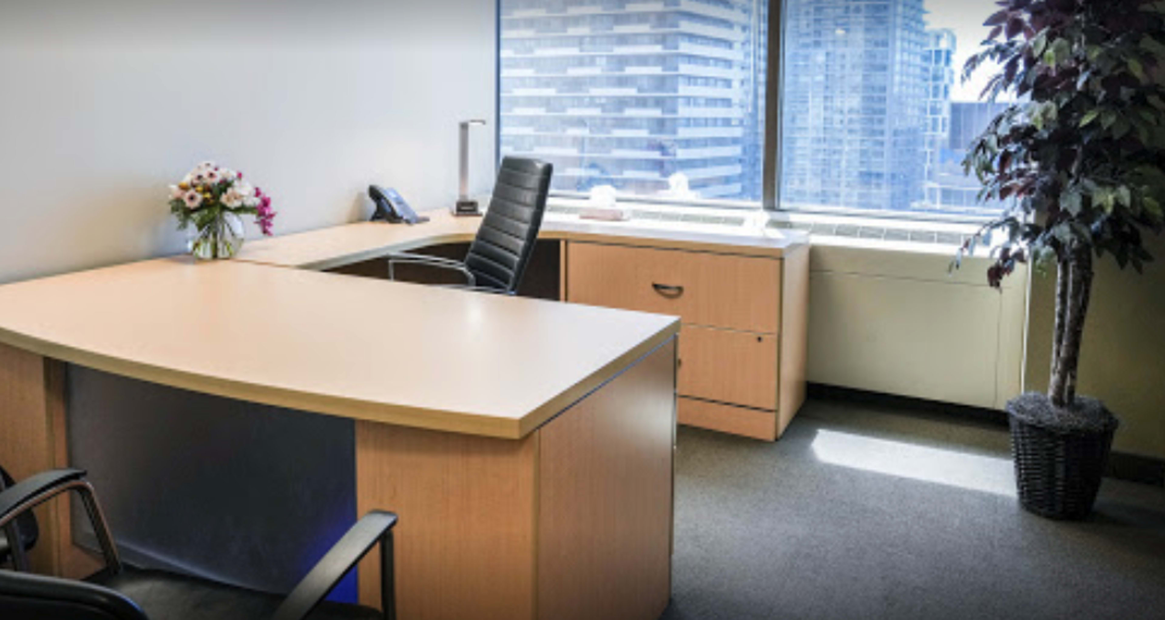 A modern office space with a large desk, a black office chair, and a window overlooking a cityscape.