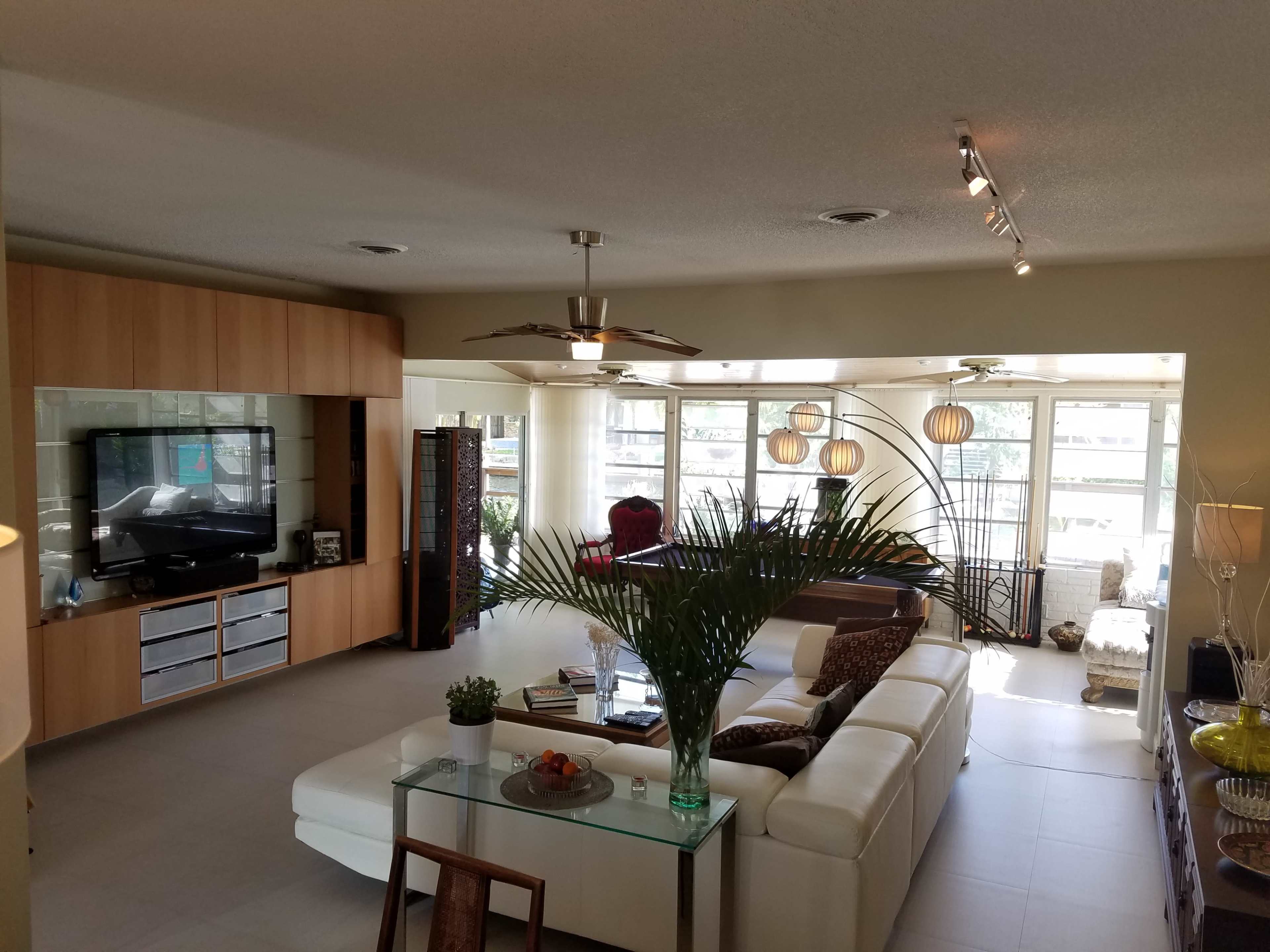 A spacious living room features modern furniture, a flat-screen TV, and large windows allowing natural light to fill the space.