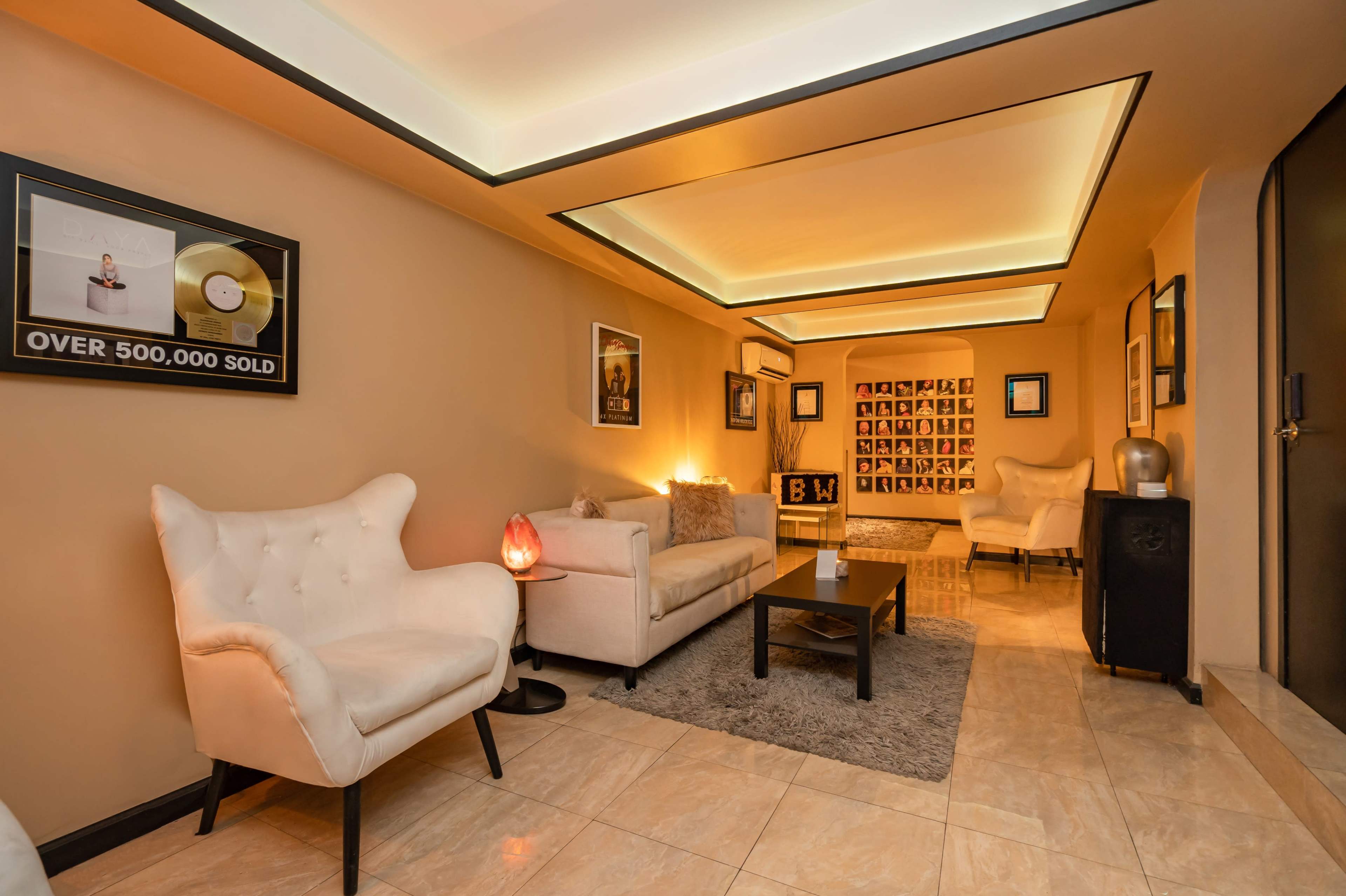 A modern living room with beige walls, two white chairs, a gray rug, a coffee table, and framed pictures on the walls.