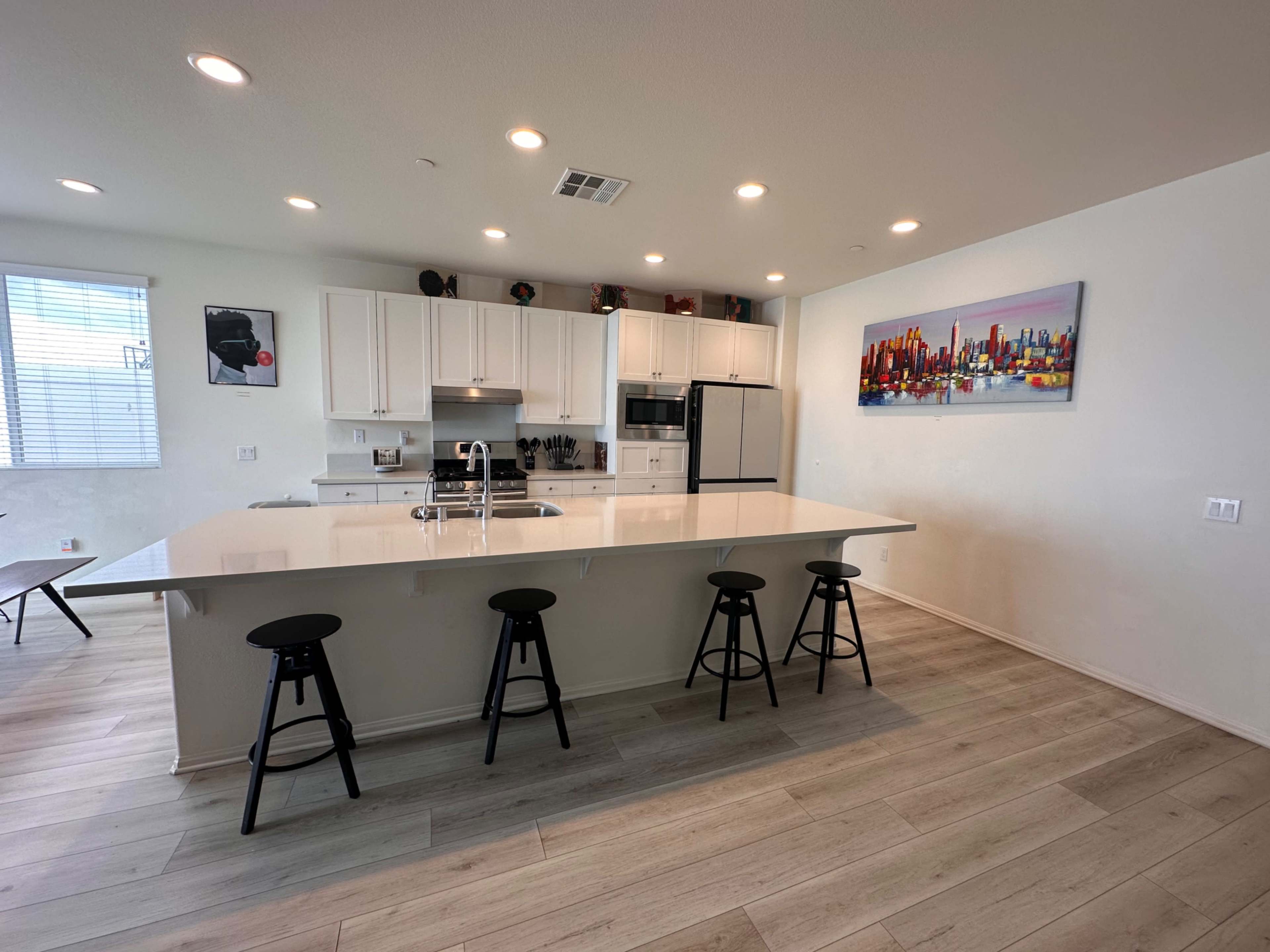A modern kitchen features white cabinetry, a central island with seating, stainless steel appliances, and a vibrant cityscape painting on the wall.