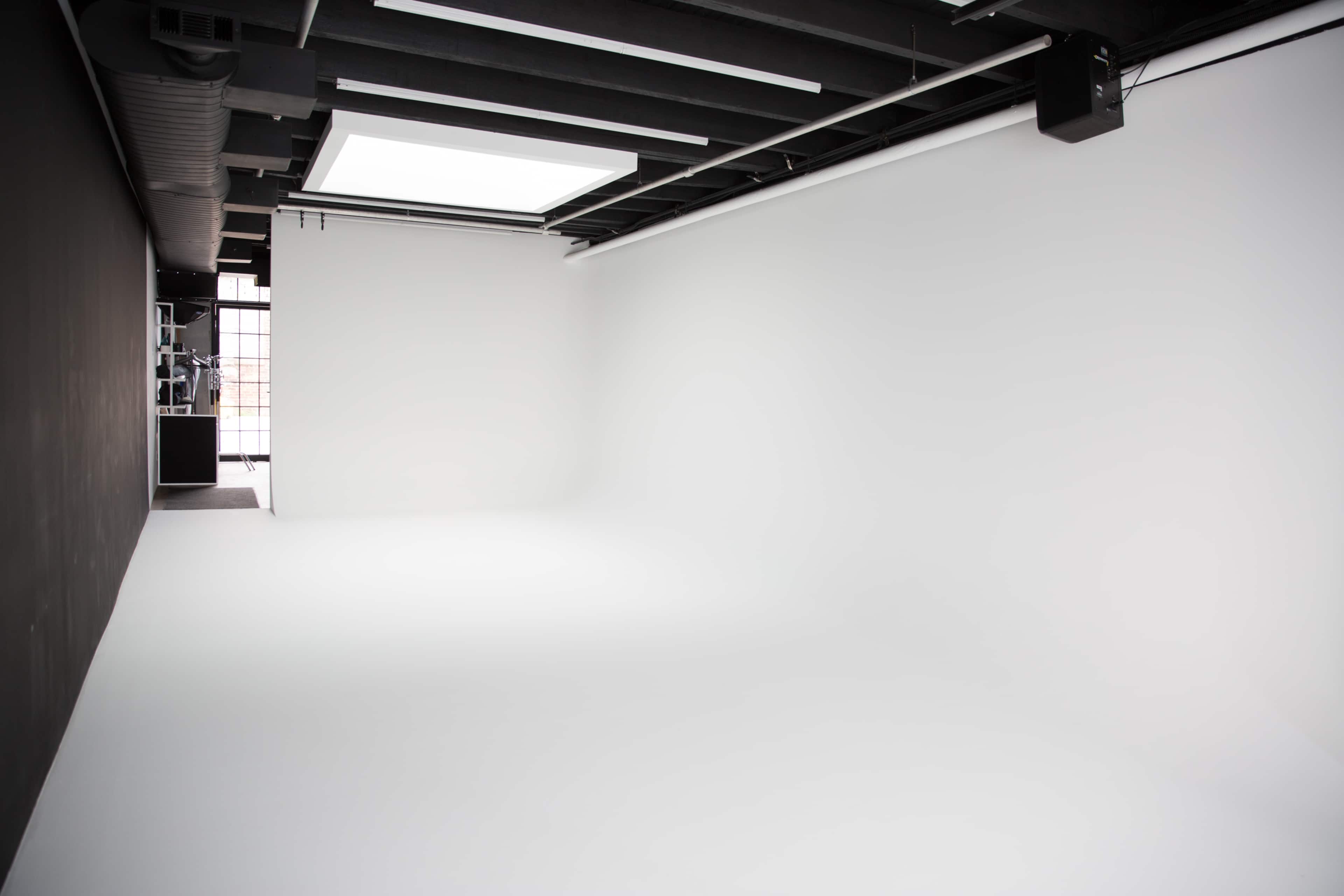 A spacious, empty photography studio with white walls and a large window letting in natural light.