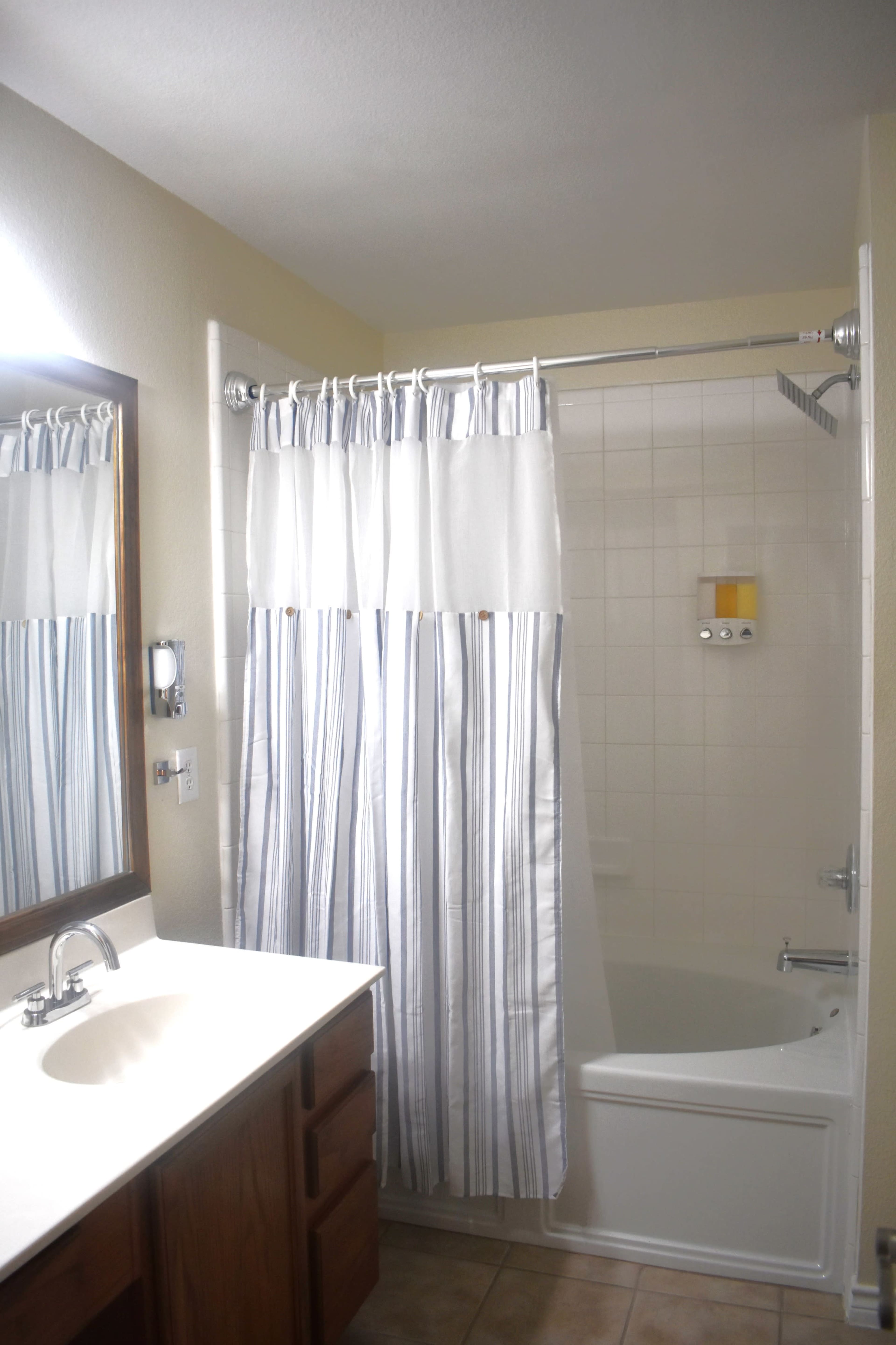 The image shows a bathroom with a bathtub, a shower curtain with stripes, a mirror above the sink, and wooden cabinets.