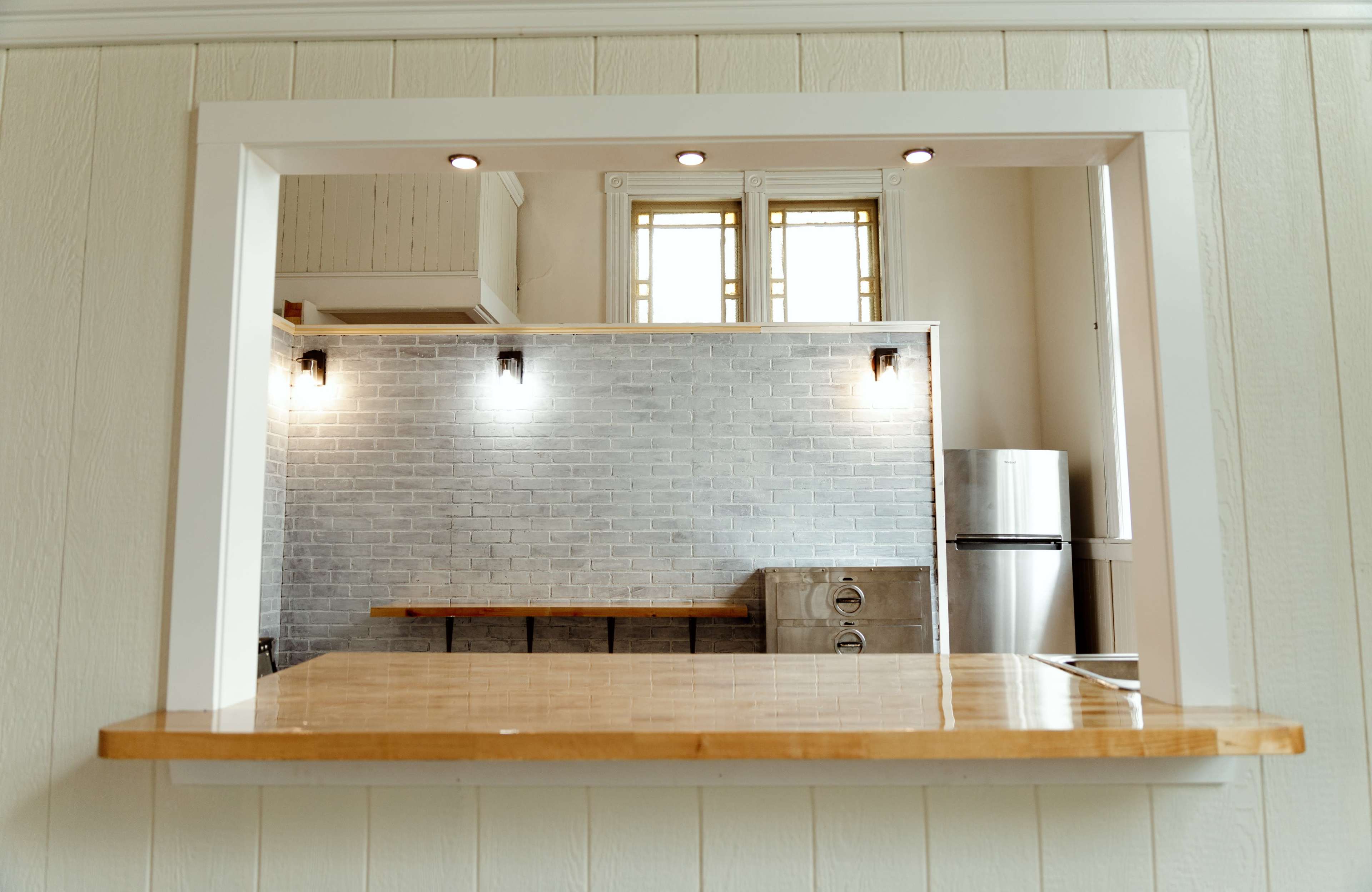 A kitchen with a wooden countertop and a grey brick wall, featuring a stainless steel refrigerator and overhead lighting.