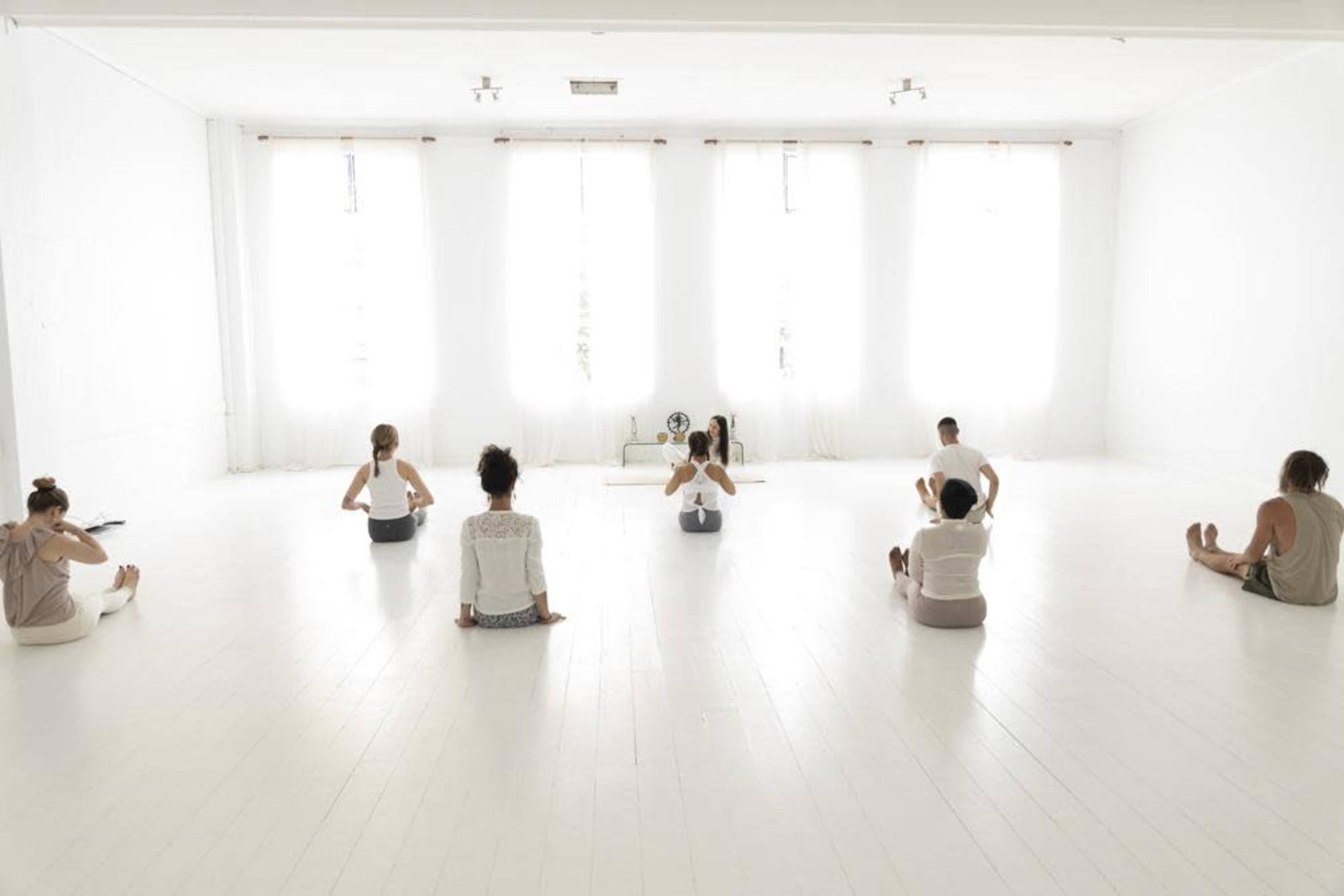 A group of individuals practices yoga in a bright, minimalist studio with large windows and wooden flooring.