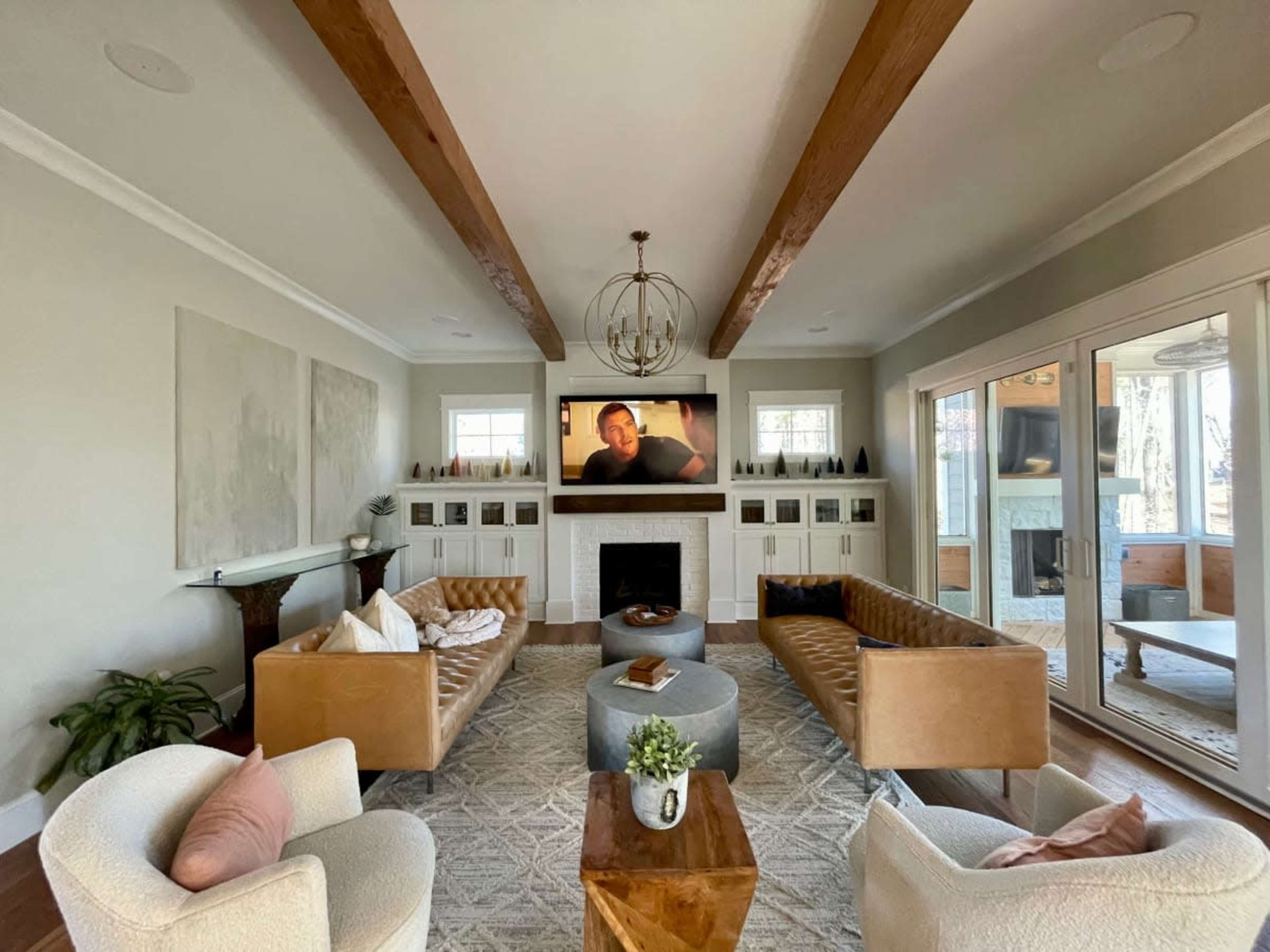 The living room features two leather sofas facing a television mounted above a fireplace, with a coffee table and a plant in the center.