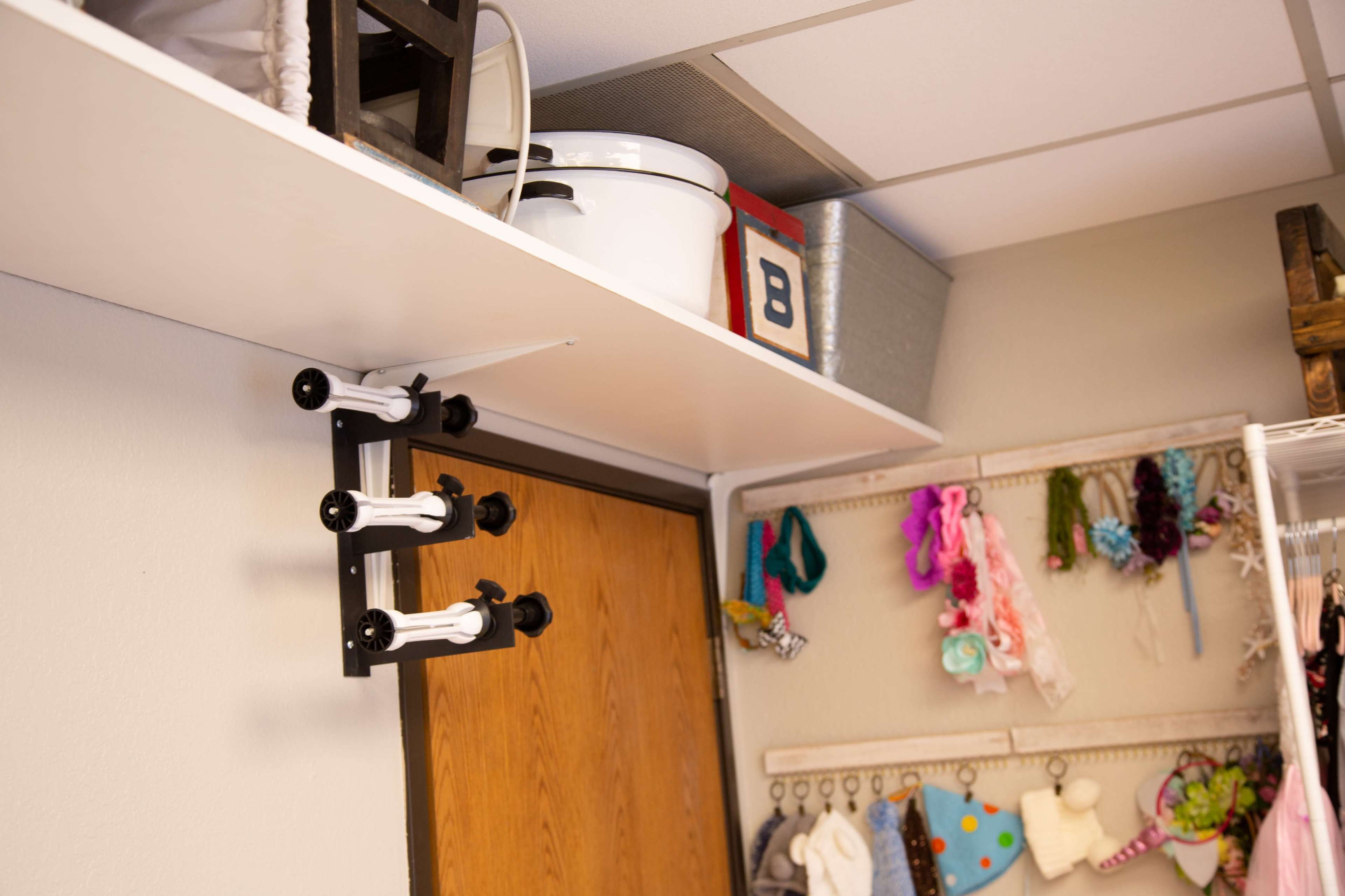 A shelf mounted above a door stocked with storage containers and a clothing rack displaying various accessories and items.