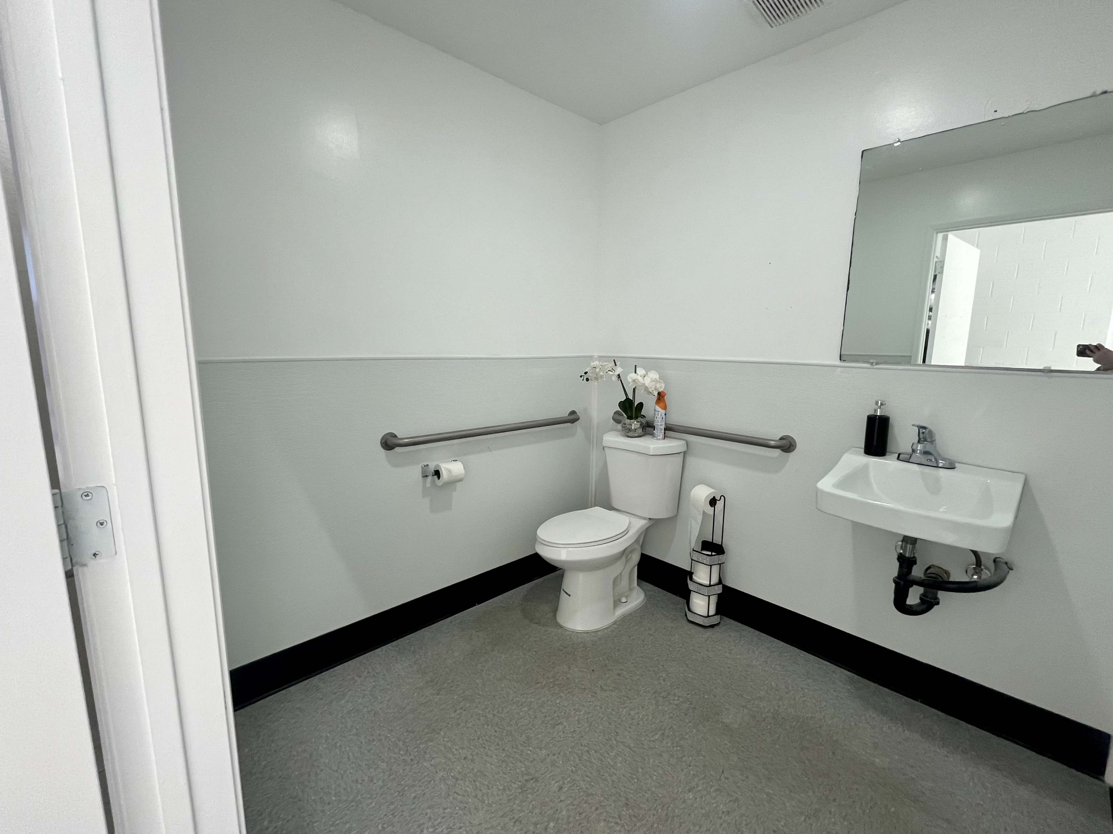 A small, clean restroom with a toilet, sink, and grab bars on the walls.