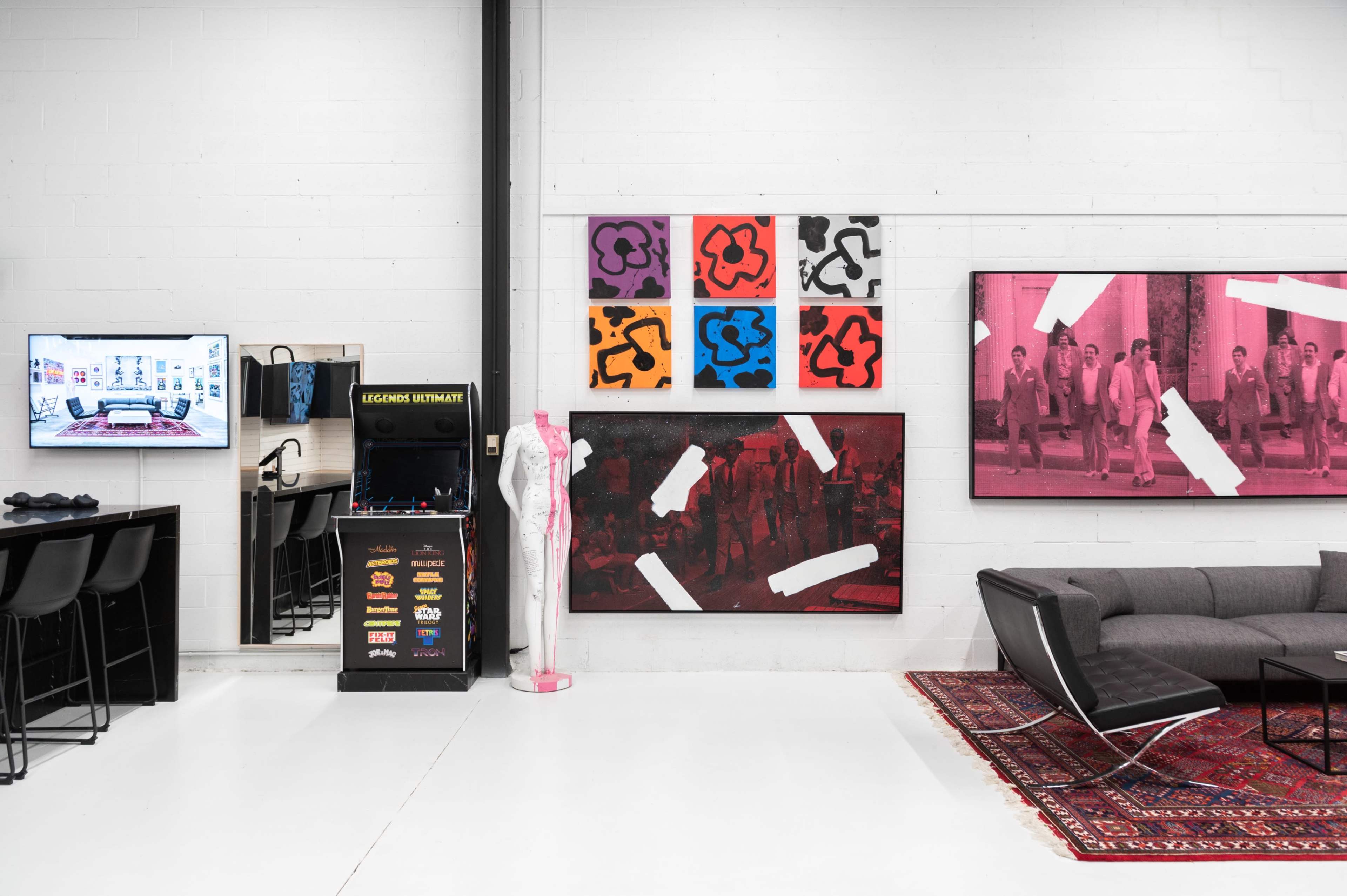 A modern workspace featuring a large wall adorned with colorful artwork, a black display unit, a television, and contemporary furniture arranged in an open layout.
