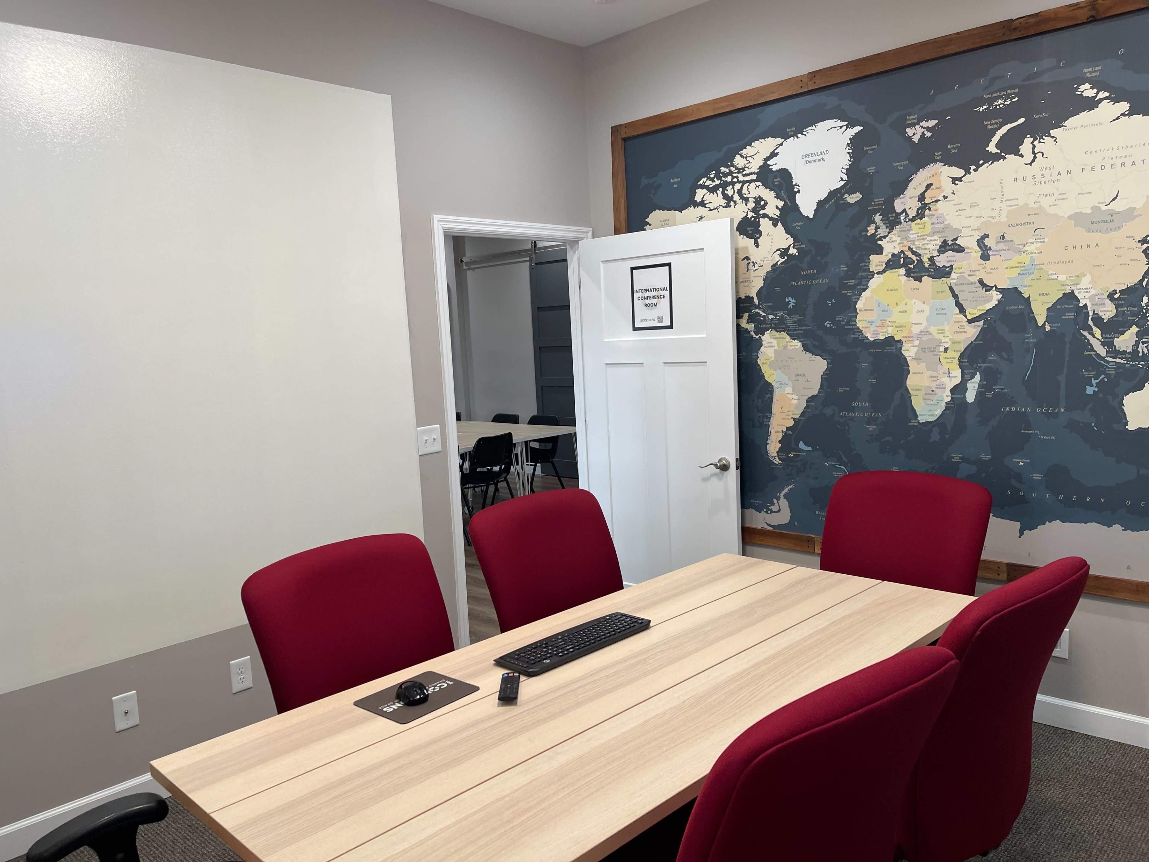 A conference room features a wooden table with four red chairs and a world map mural on the wall.