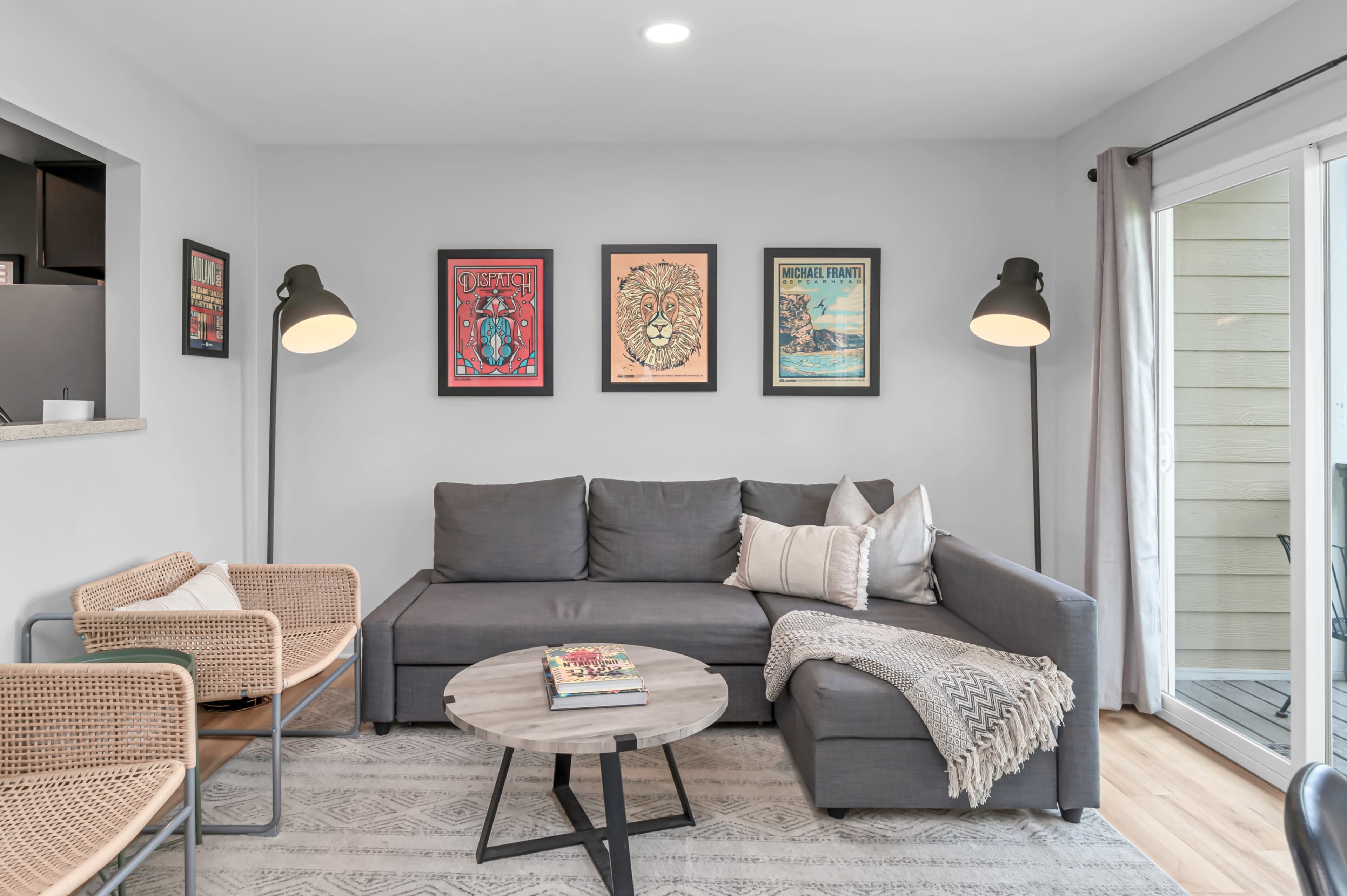 A modern living room with a gray sectional sofa, two woven chairs, a round coffee table, and framed artwork on the walls.