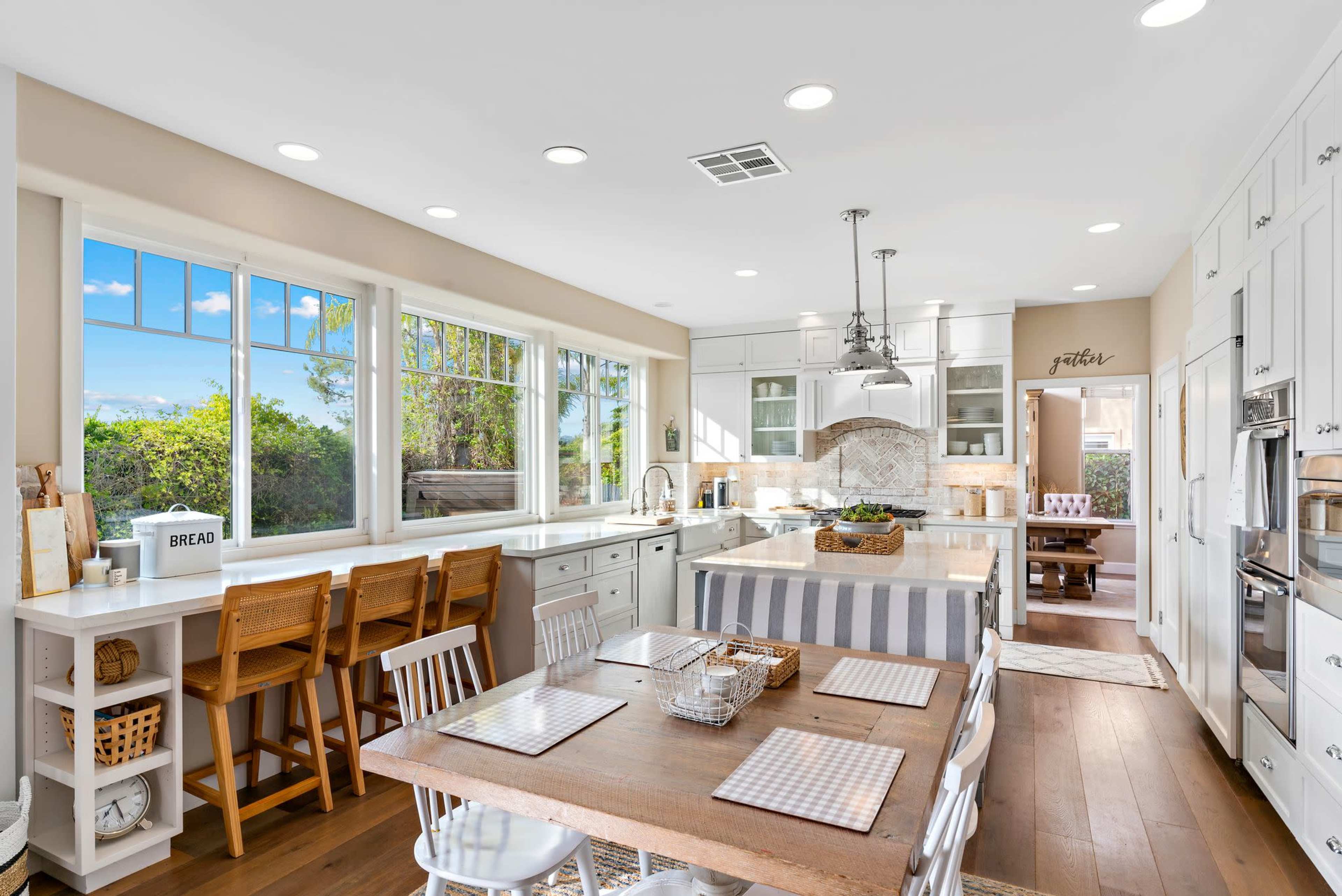 A spacious kitchen features a central island, white cabinetry, and a dining area with a wooden table and chairs.