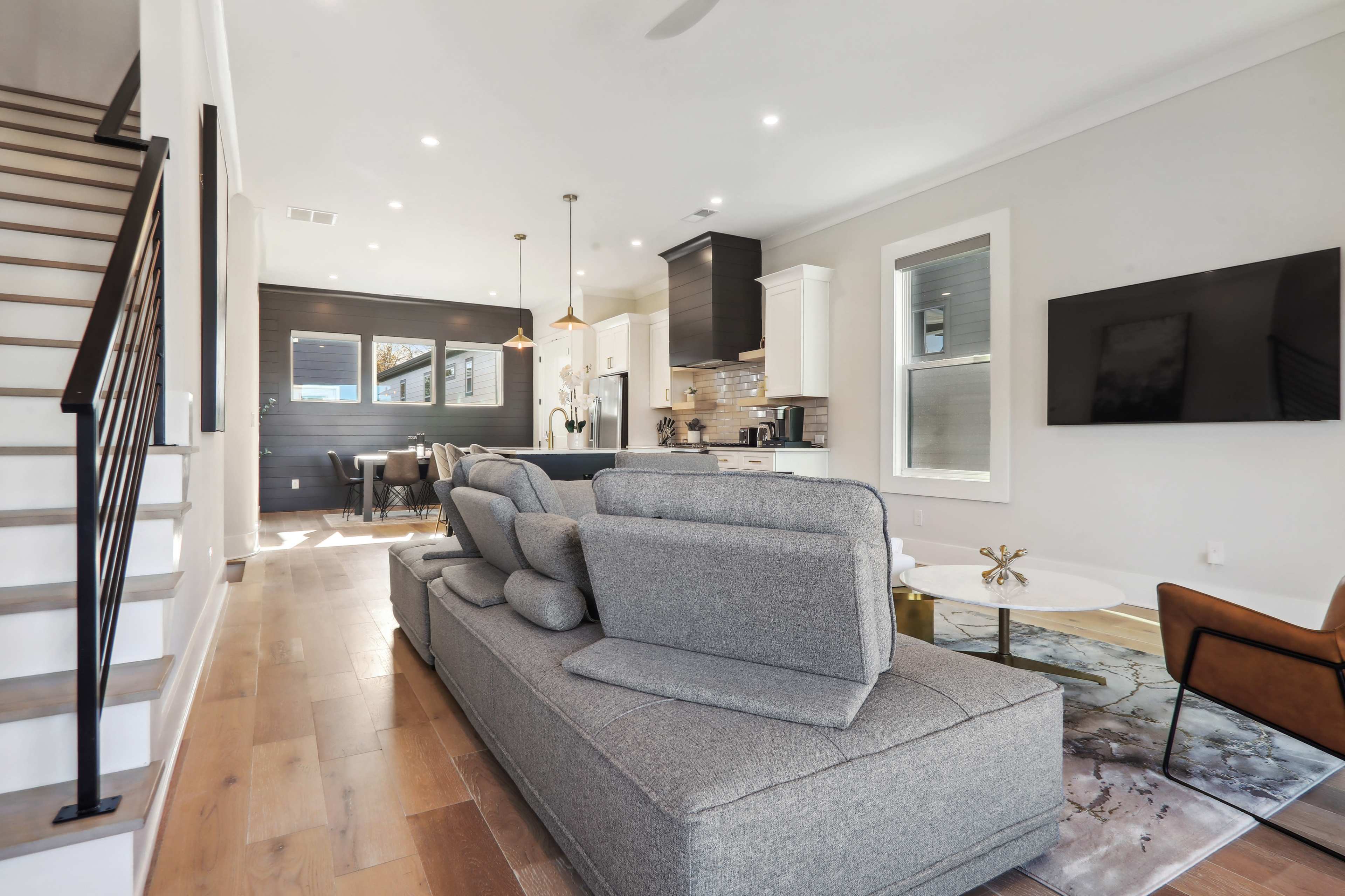 A modern, open-concept living area with a gray sofa, wooden flooring, and a staircase leading to an upper level.