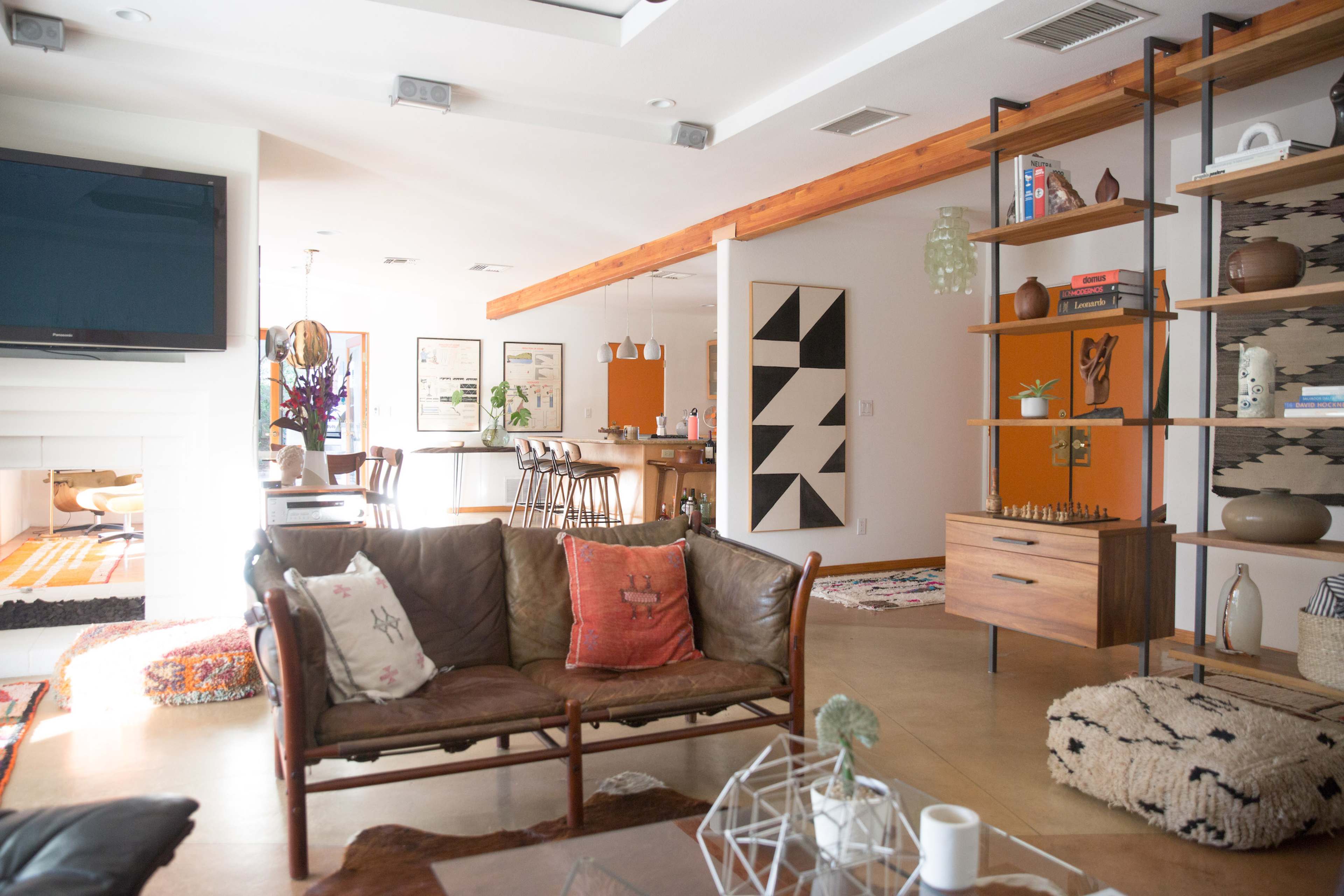 A modern living space featuring a leather couch, a wooden coffee table, and shelves filled with decor, along with an open kitchen area in the background.