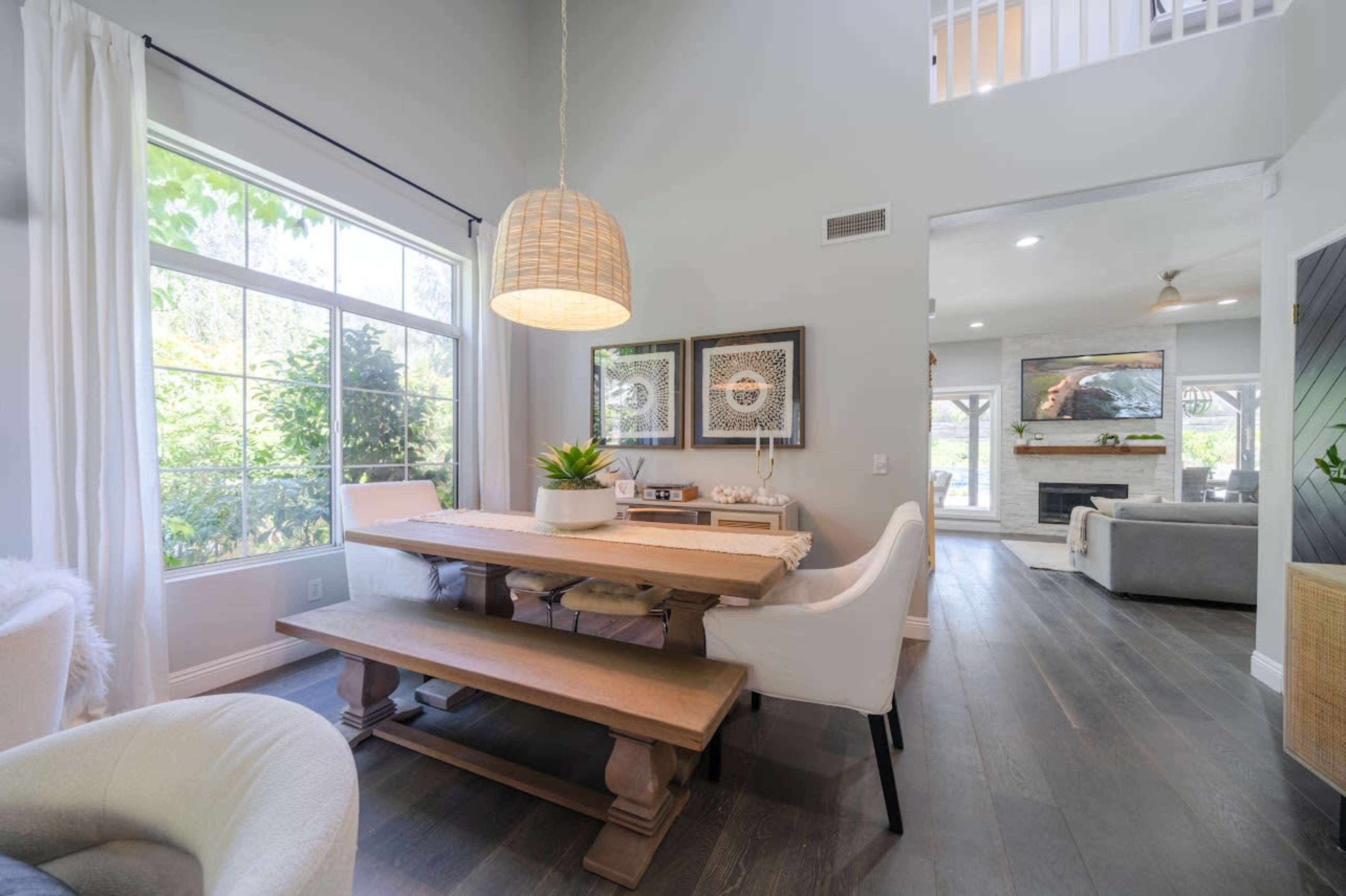 A modern dining area with a wooden table and chairs, large windows allowing natural light, and a light fixture hanging overhead.