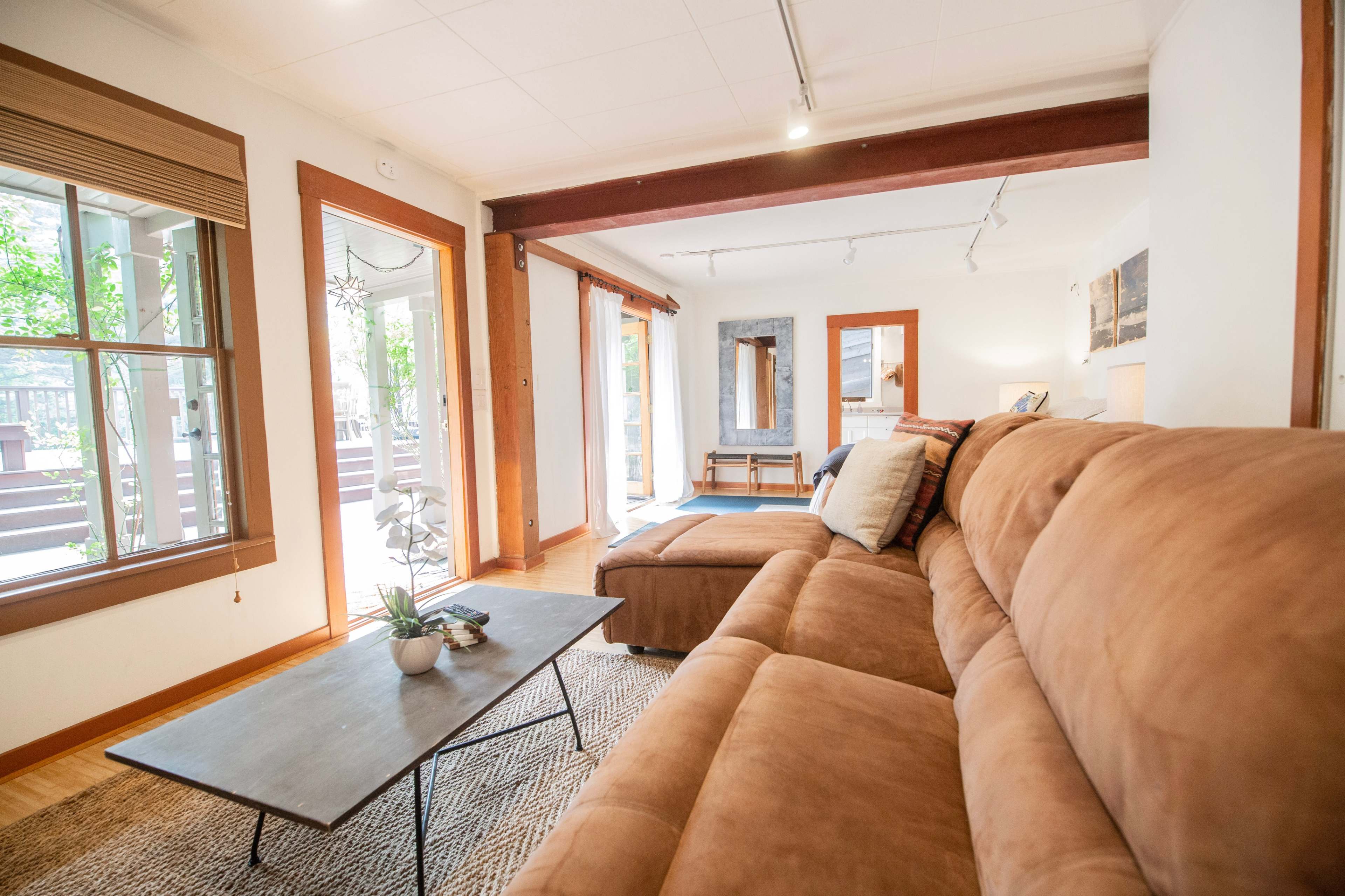 A spacious living room features a brown sectional sofa, a coffee table, and large windows letting in natural light.