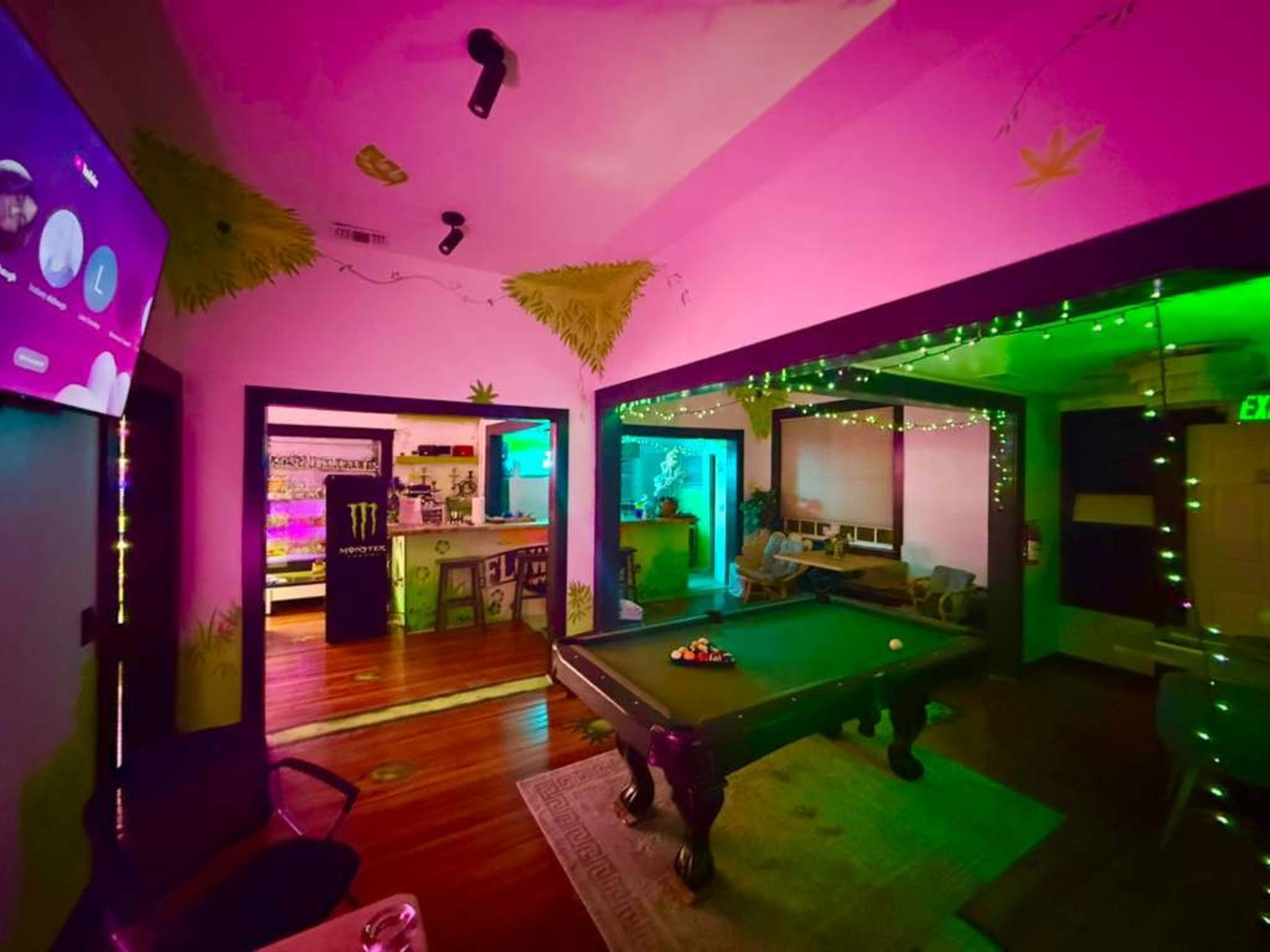 The image shows a brightly colored room with a pool table, adorned with neon lights and wall decorations featuring cannabis leaves.