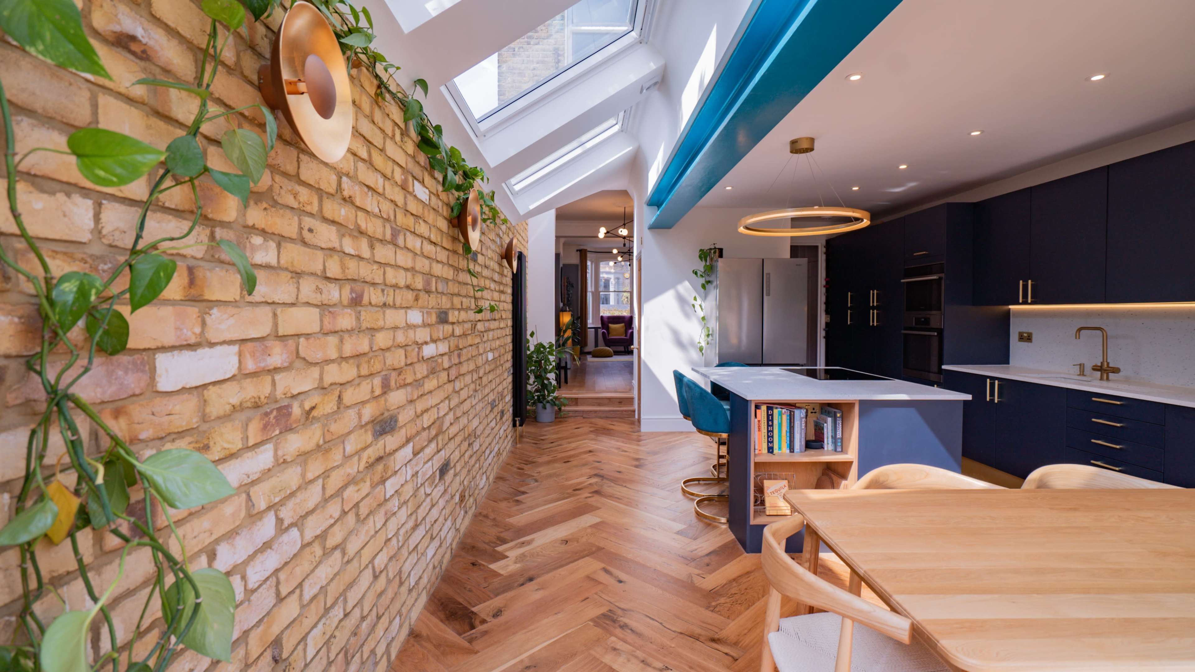 A modern kitchen and dining area with a brick wall, skylights, and wooden flooring.