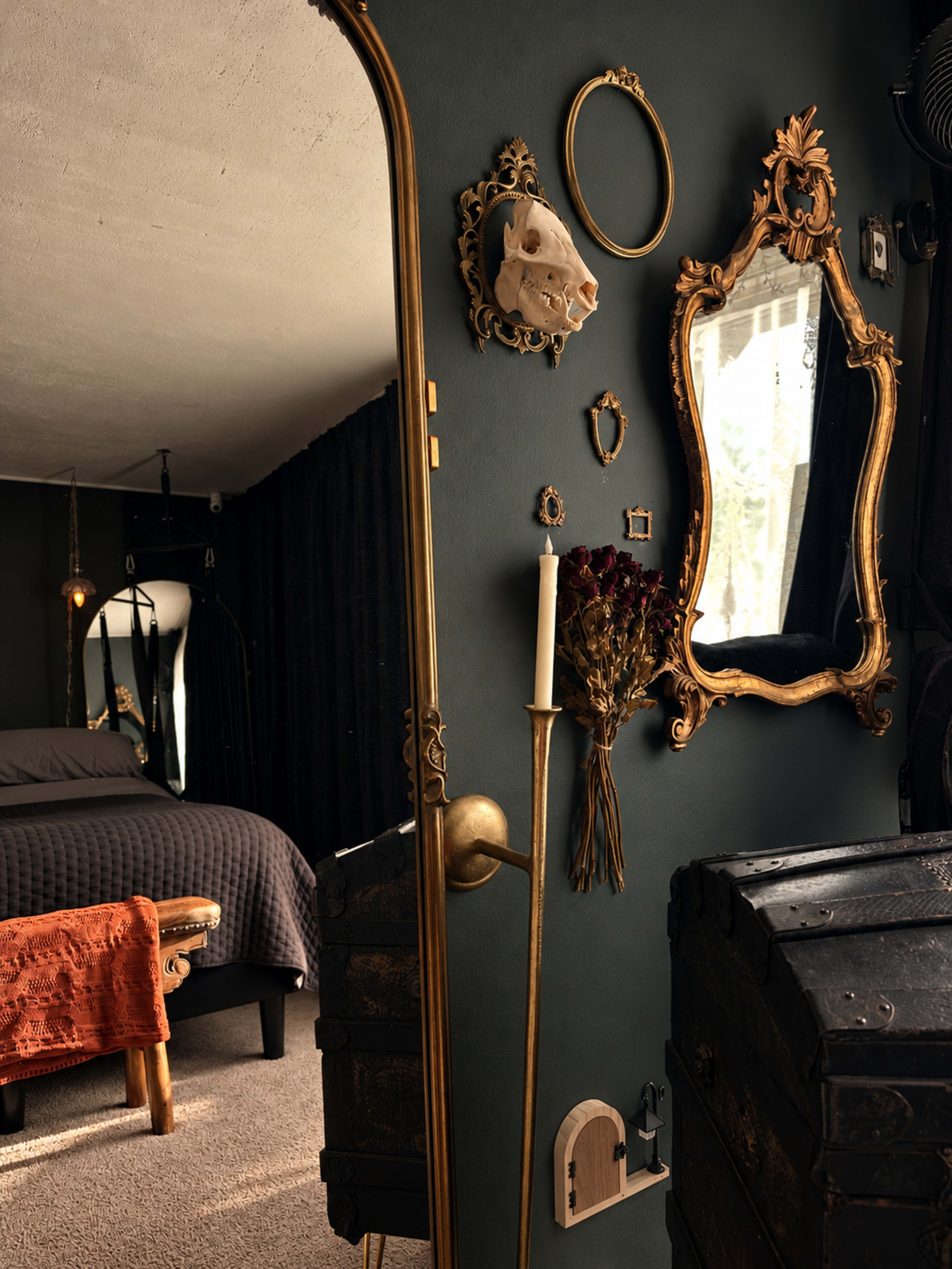 The image shows a dimly lit bedroom featuring a large mirror framed in ornate gold, a neatly made bed with a gray duvet, and an assortment of decorative items on the walls.