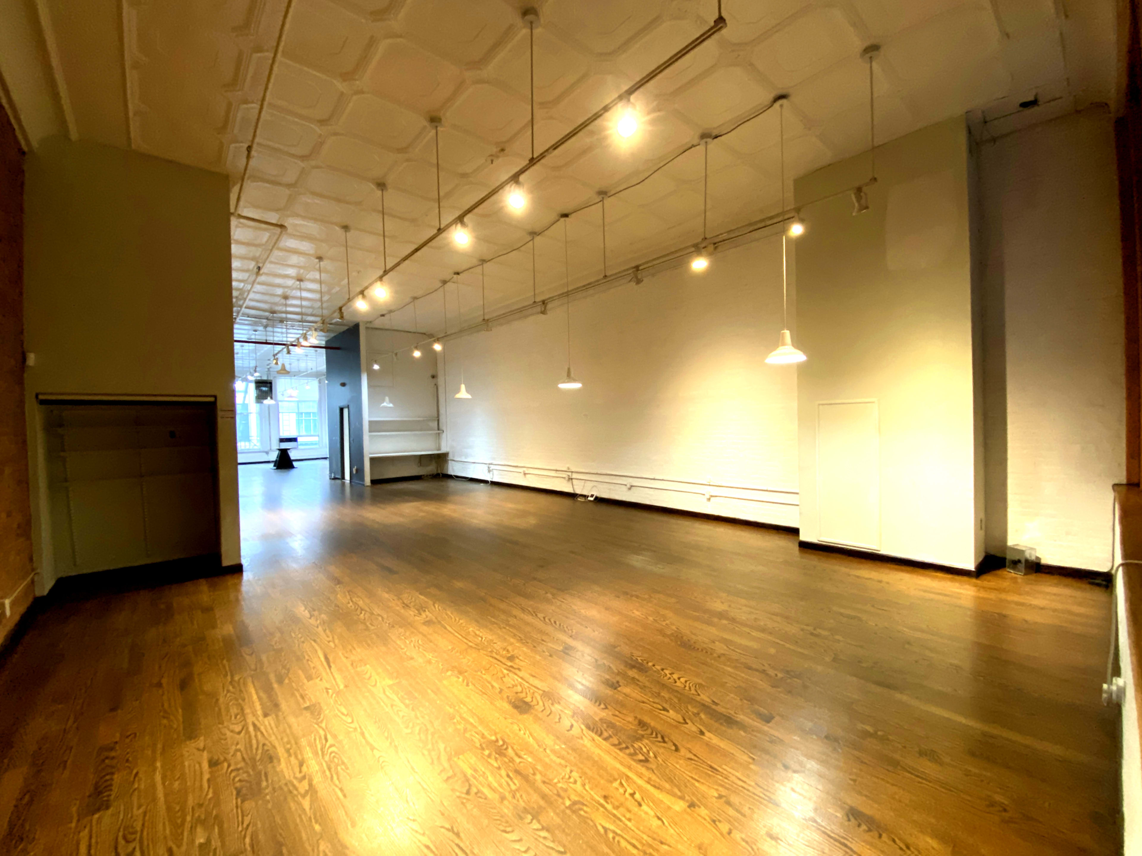 A spacious, empty room with hardwood floors, white walls, and pendant lighting.