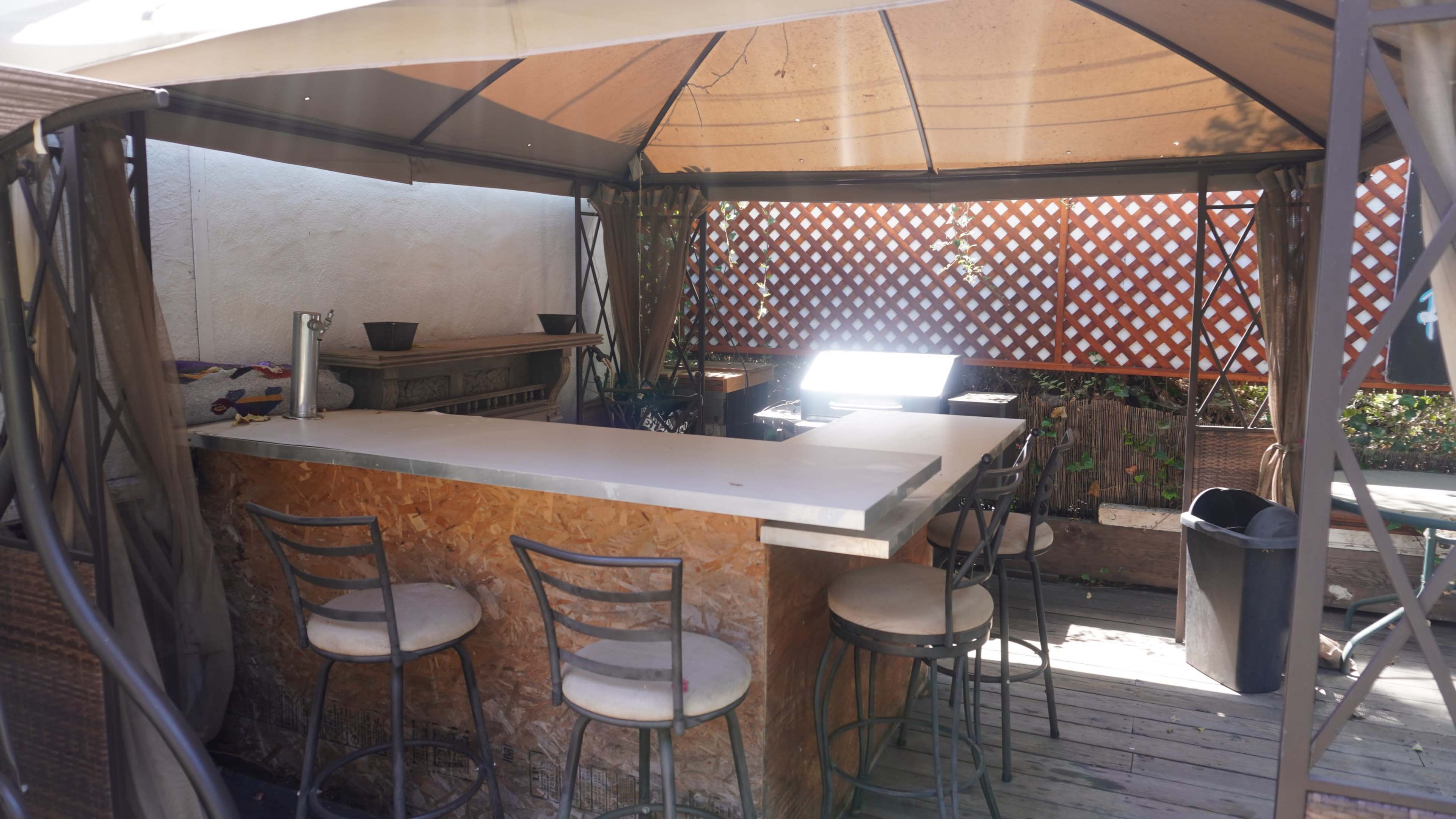 An outdoor bar area with a counter, several stools, and a lattice privacy screen.